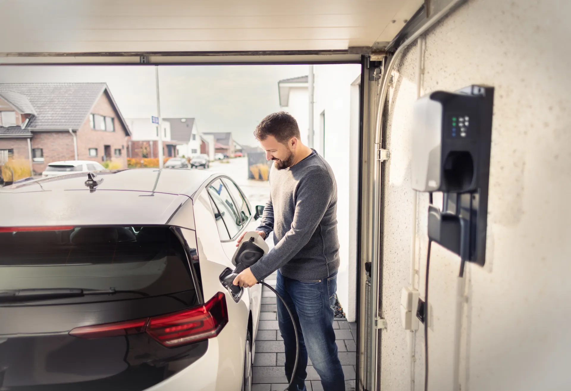 Ein Mann lädt sein weißes Elektroauto mit seiner Wallbox in der Garage auf.