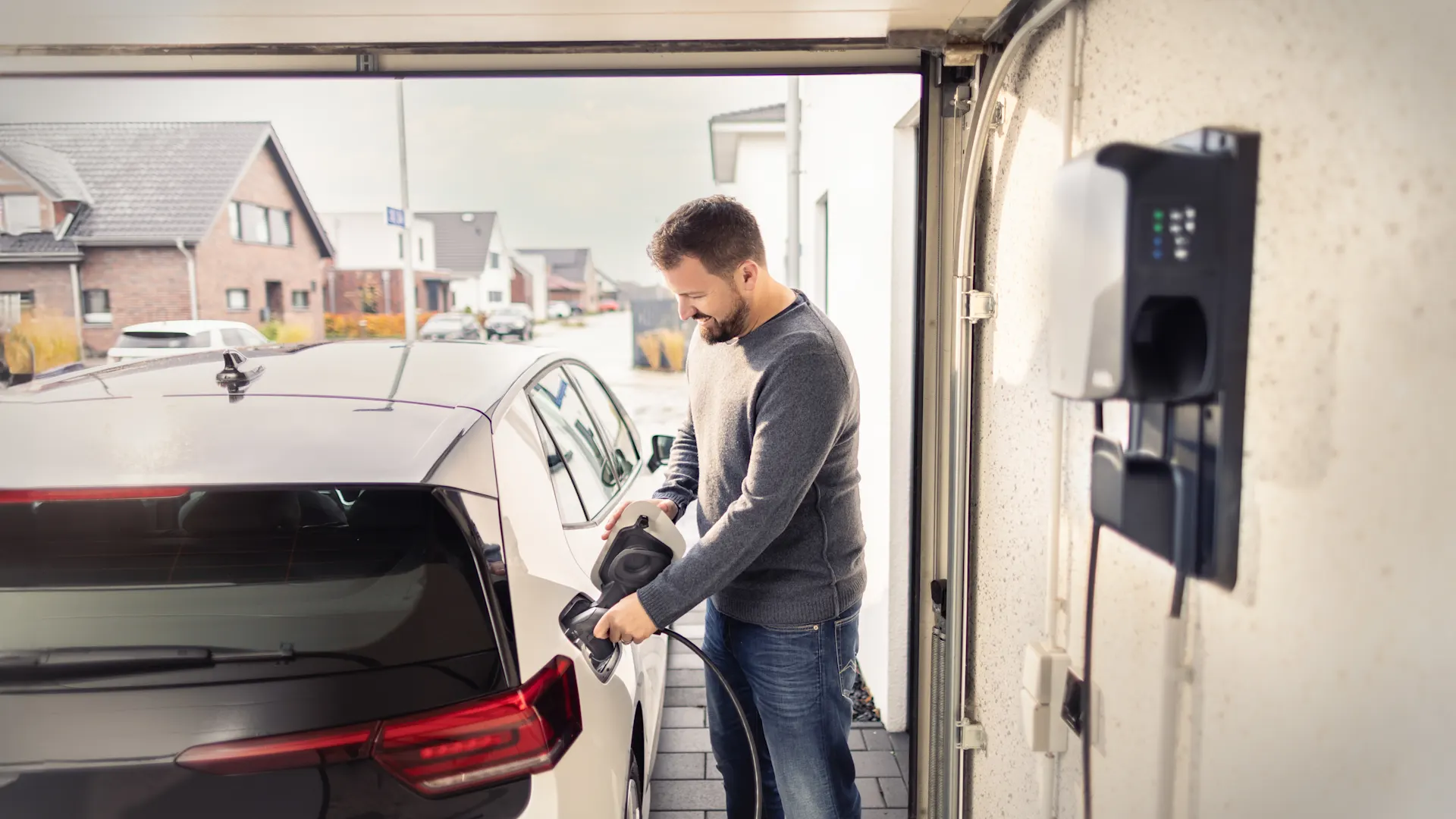 Ein Mann lädt sein Elektroauto mit seiner Wallbox auf. Ein Mann lädt sein weißes Elektroauto mit seiner Wallbox in der Garage auf.
