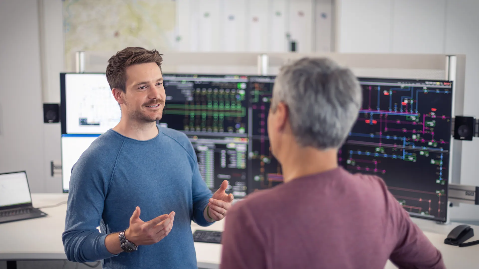 Zwei Mitarbeiter in der Netzleitstelle Zwei Mitarbeiter stehen in der Netzleitstelle und unterhalten sich.