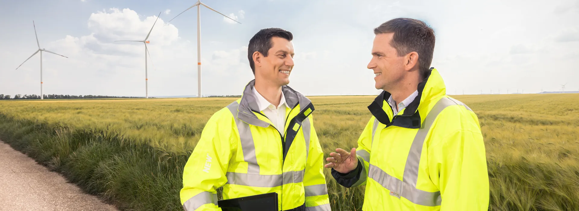 Fachpartner der NEW Netz unterhalten sich. Zwei Fachpartner der NEW Netz stehen vor einer Windkraftanlage