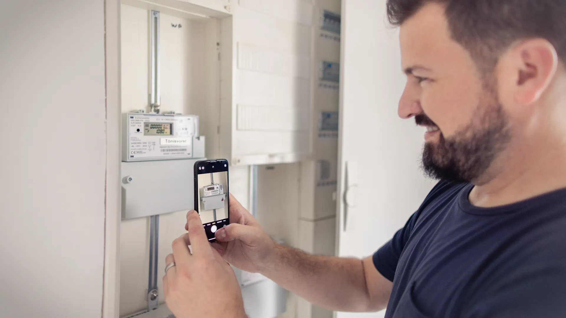 Ein Mann macht ein Foto einer modernen Messeinrichtung. Ein Mann fotografiert mit seinem Handy eine moderne Messeinrichtung, die bei ihm zu Hause installiert ist.