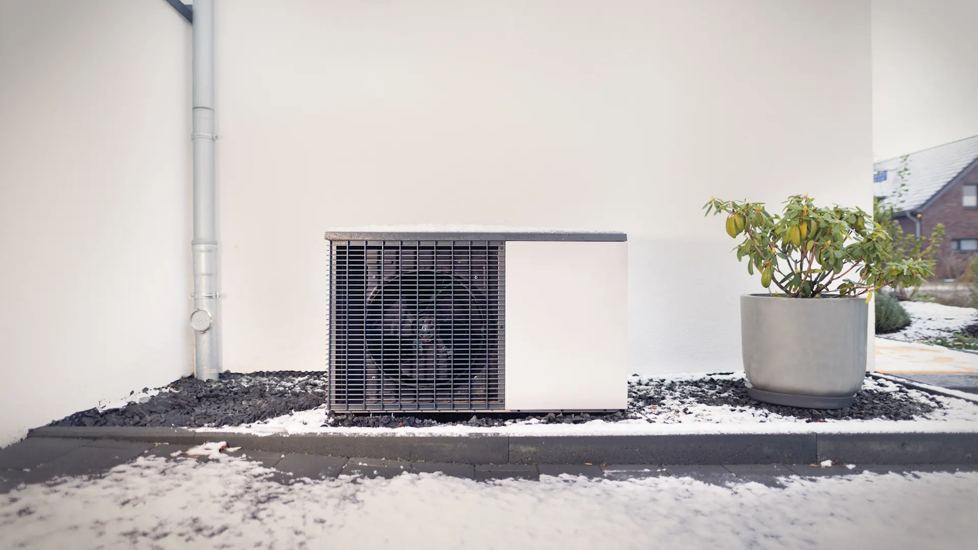 Eine Wärmepumpe, die außen vor einem Haus installiert ist. Ein moderne Wärmepumpe steht neben einer schlichten weißen Hauswand.