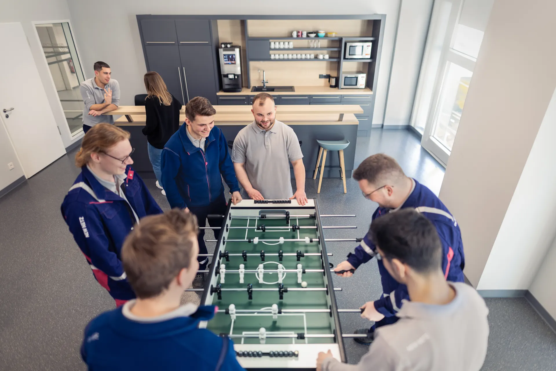 Fünf Auszubildene der NEW Netz stehen um einen Kickertisch und genießen ihre Mittagspause beim Kickern in den Werkstätten der NEW Netz.
