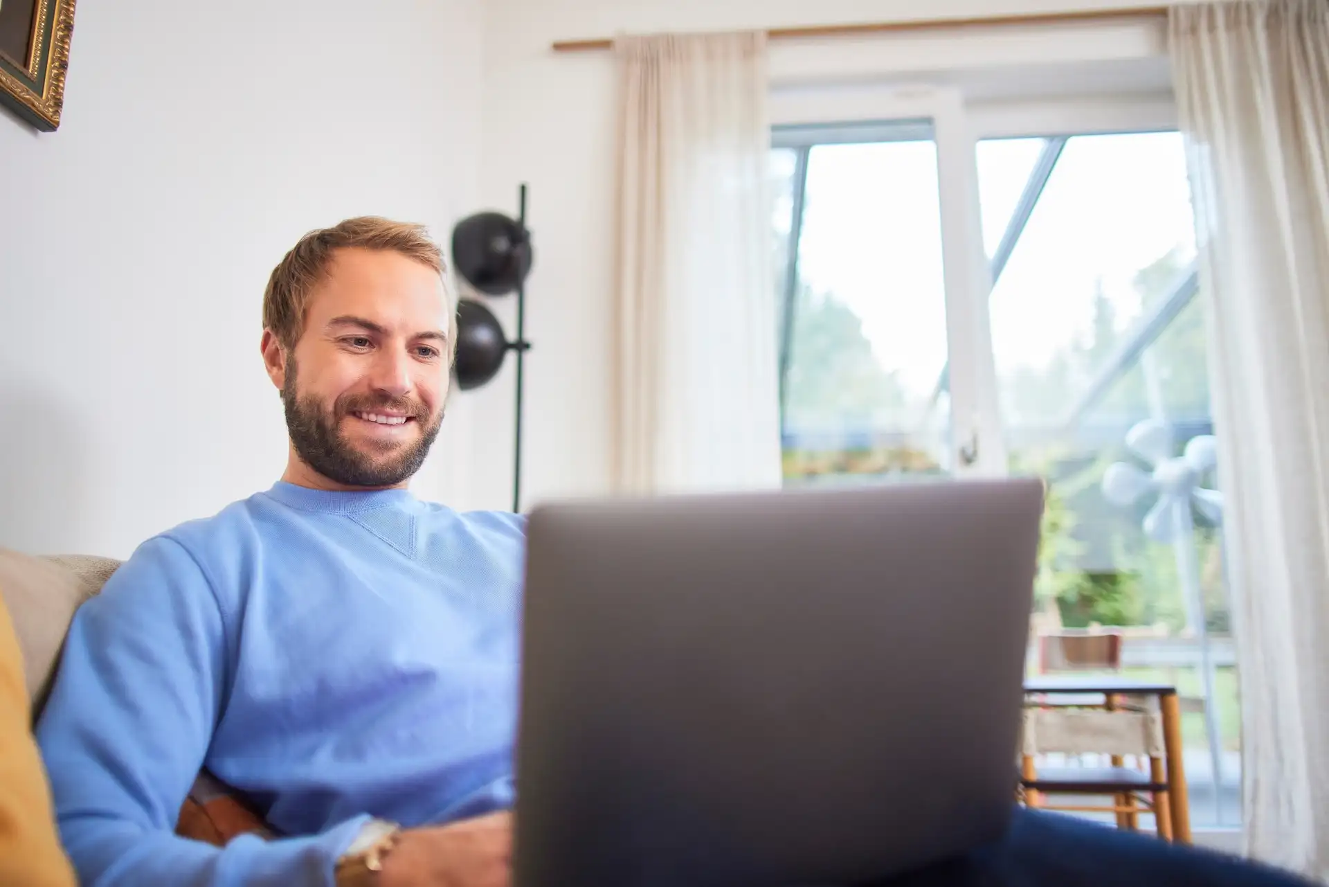 Ein Mann sitzt auf der Couch an seinem Laptop und ist auf der NEW Netz Website