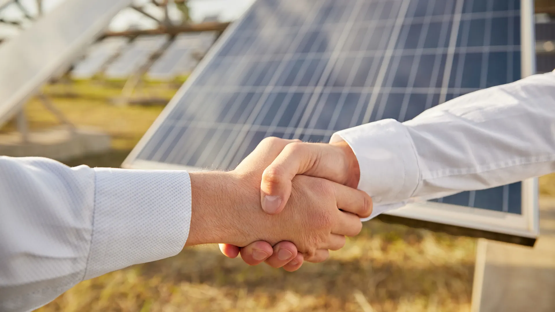Handschlag vor Solaranlagenpark Zwei Geschäftspartner geben sich die Hand. Im Hintergrund ist ein Solarpark angedeutet.