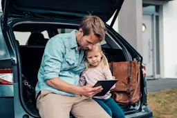 Auswahl eines Ladevorgangs Vater und Kind sitzen zusammen im Kofferraum und beobachten den Ladevorgang ihres E-Autos.