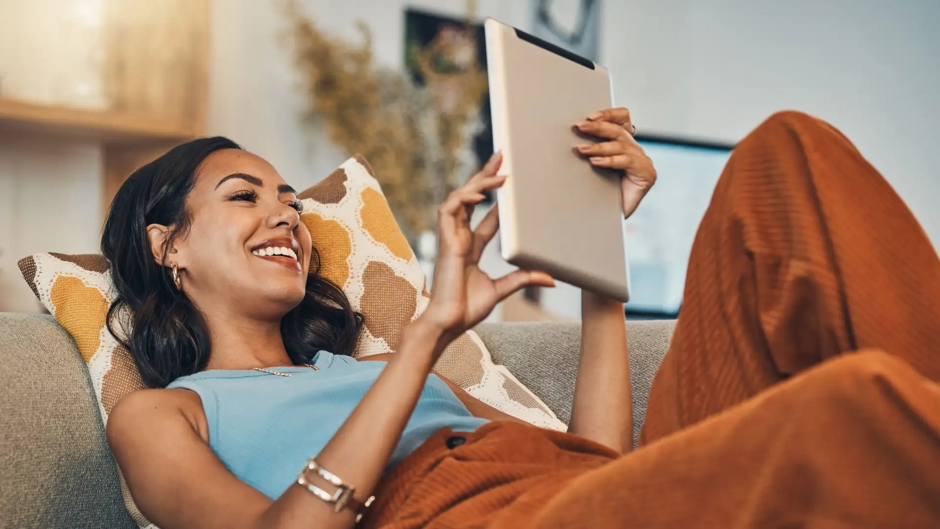 Eine Junge Frau liegt mit dem Tablet auf der Couch und erkundigt sich nach günstigem Strom der NEW Energie.