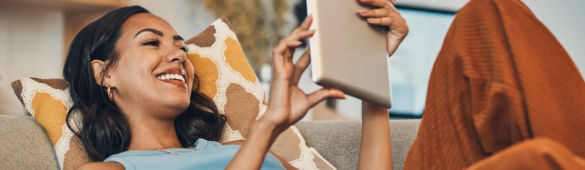 Auswahl von günstigem Strom Eine junge Frau liegt mit dem Tablet auf der Couch und erkundigt sich nach günstigem Strom der NEW Energie.