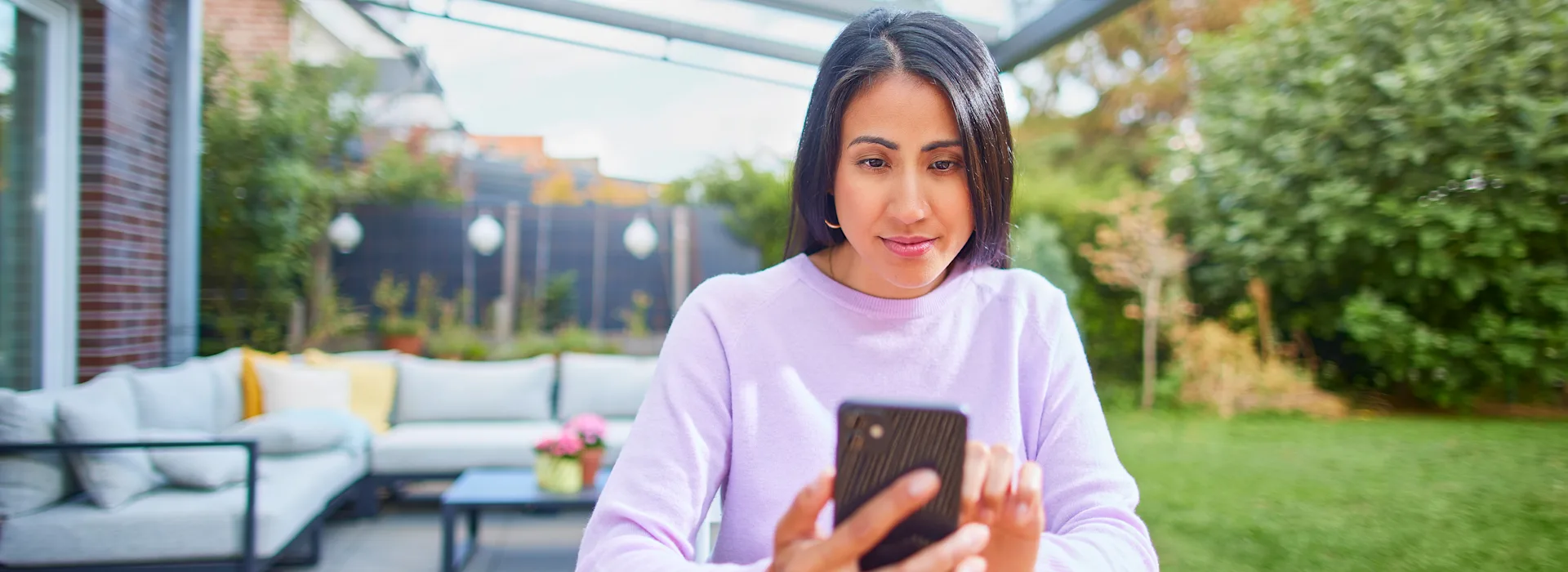 NEW Dienstleistungen Eine Frau sitzt im Garten mit ihrem Smartphone und informiert sich über die Dienstleistungen und den Service bei der NEW Energie.