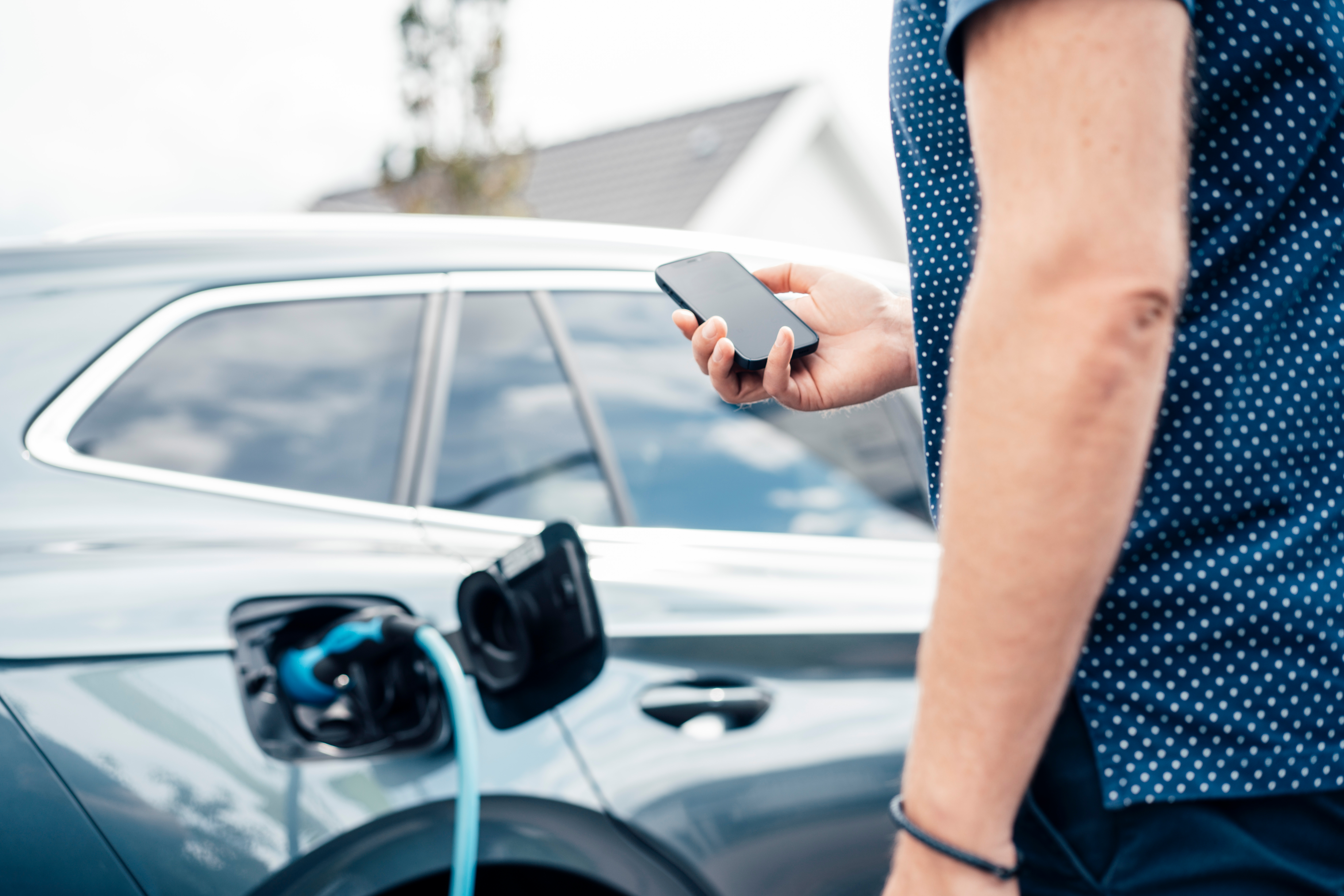 Das E-Auto hängt am Ladekabel. Ein Mann überwacht den Ladevorgang am Smartphone.