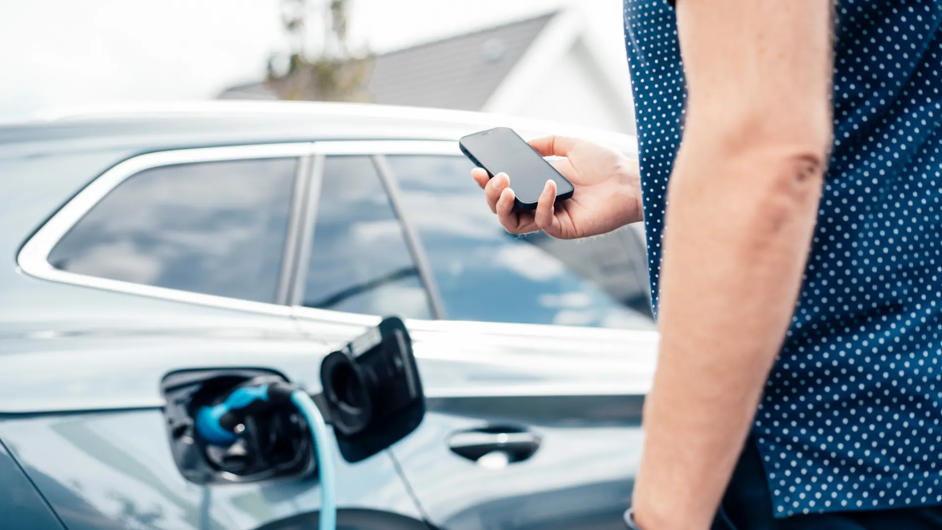 E-Laden auch unterwegs Das E-Auto hängt am Ladekabel. Ein Mann überwacht den Ladevorgang am Smartphone.