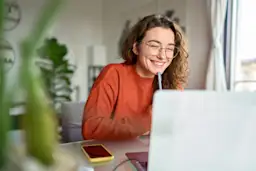 Barrierefreiheit bei der NEW Energie Frau sitzt mit einem Stift am Kinn lächelnd vor einem Laptop.