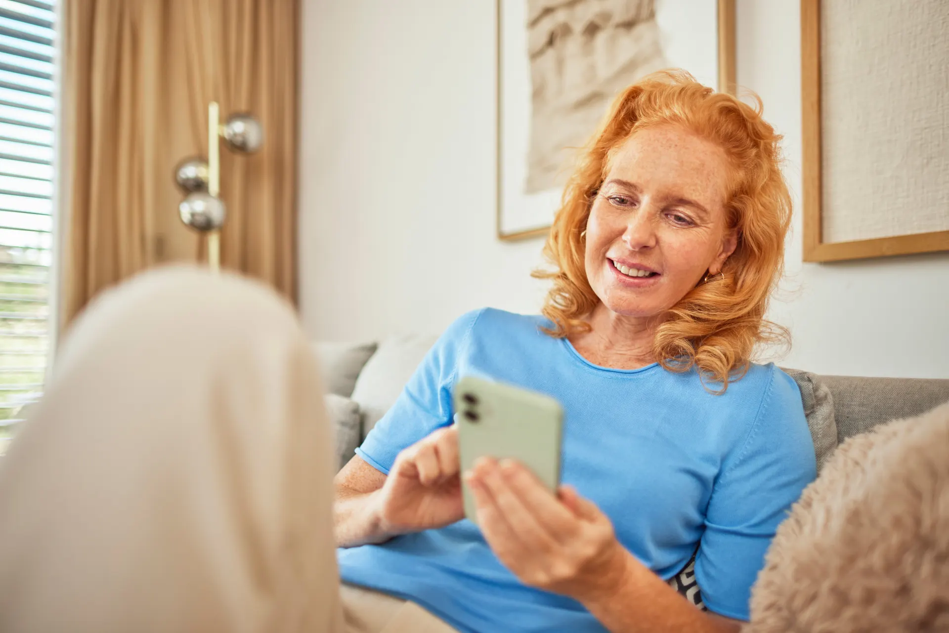 Eine Frau sitzt mit ihrem Smartphone auf dem Sofa und informiert sich über günstige Tarife, Services und Wissenswertes der NEW Energie.