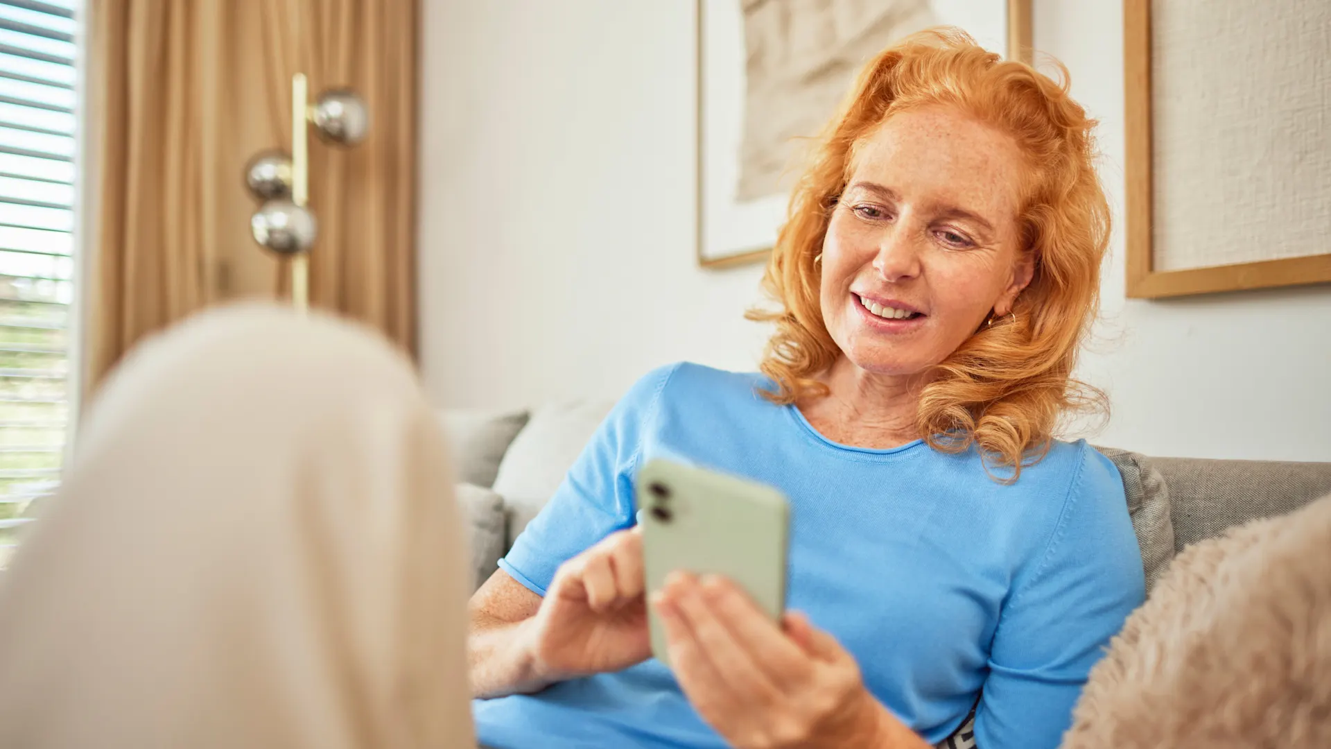 Online seine Angelegenheiten regeln Eine Frau sitzt mit ihrem Smartphone auf dem Sofa und informiert sich über günstige Tarife, Services und Wissenswertes der NEW Energie.