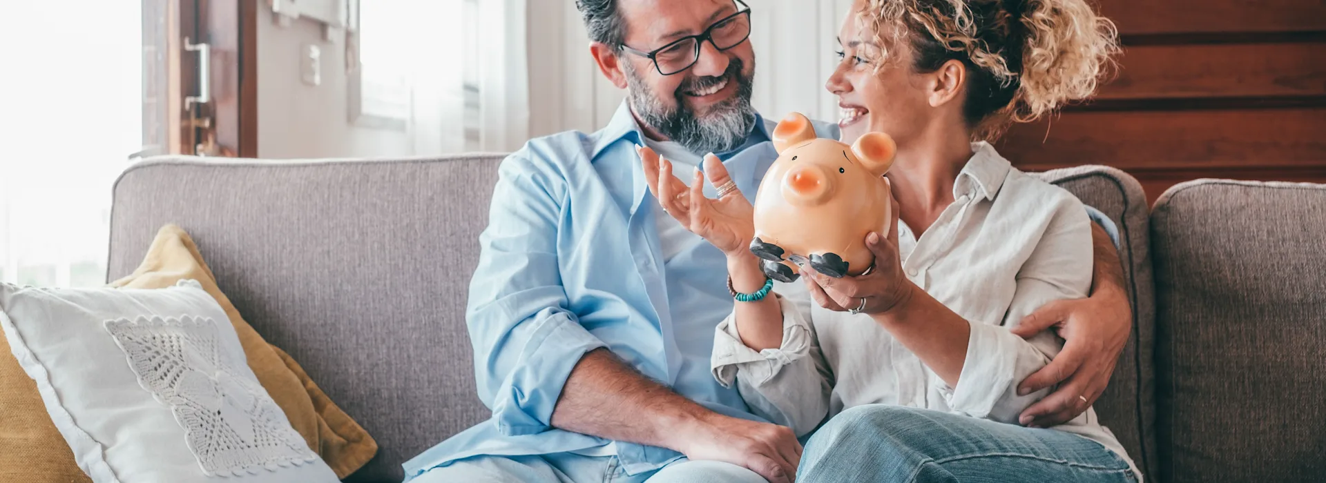 Sparen mit günstiger Energie von der NEW Energie Frau und Mann sitzen auf einer Couch und halten ein Sparschwein in der Hand.