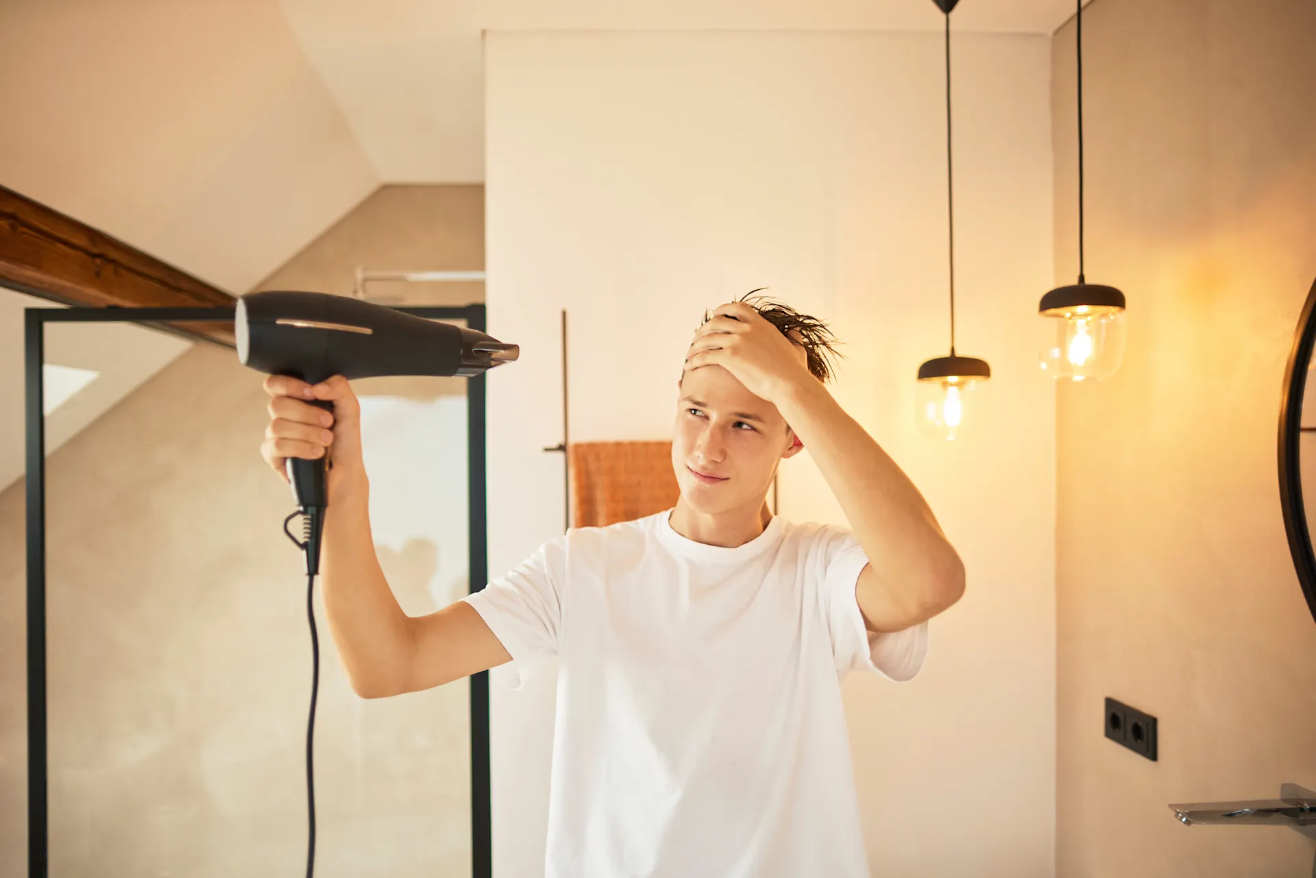 Ein junger Mann ist sich die Haare am föhnen mit Ökostrom, welcher günstigen Strom von dem Stromanbieter NEW Energie darstellt.