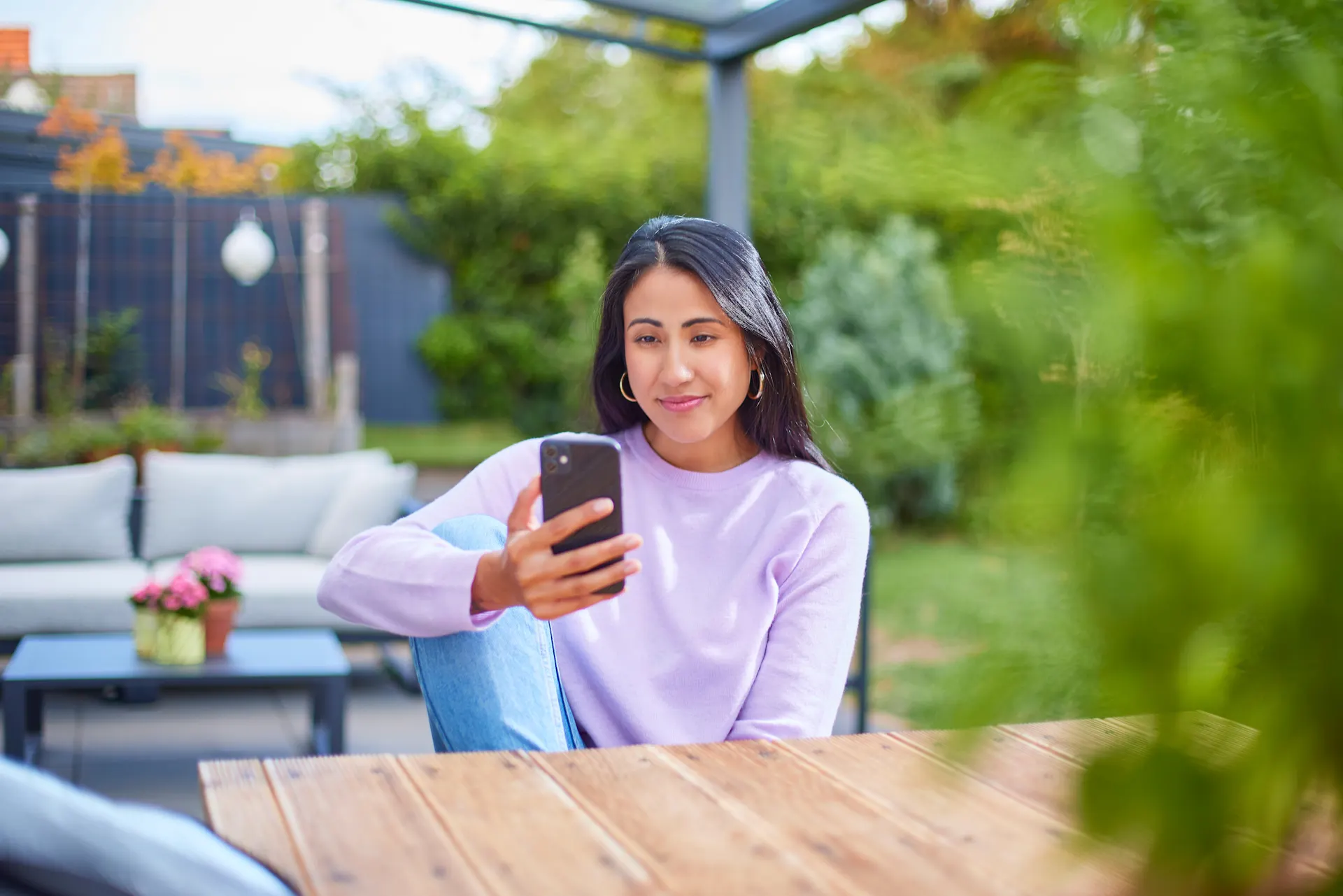Eine Frau sitzt im Garten mit einem Smartphone und informiert sich über günstige Tarife und günstige Energie der NEW Energie.