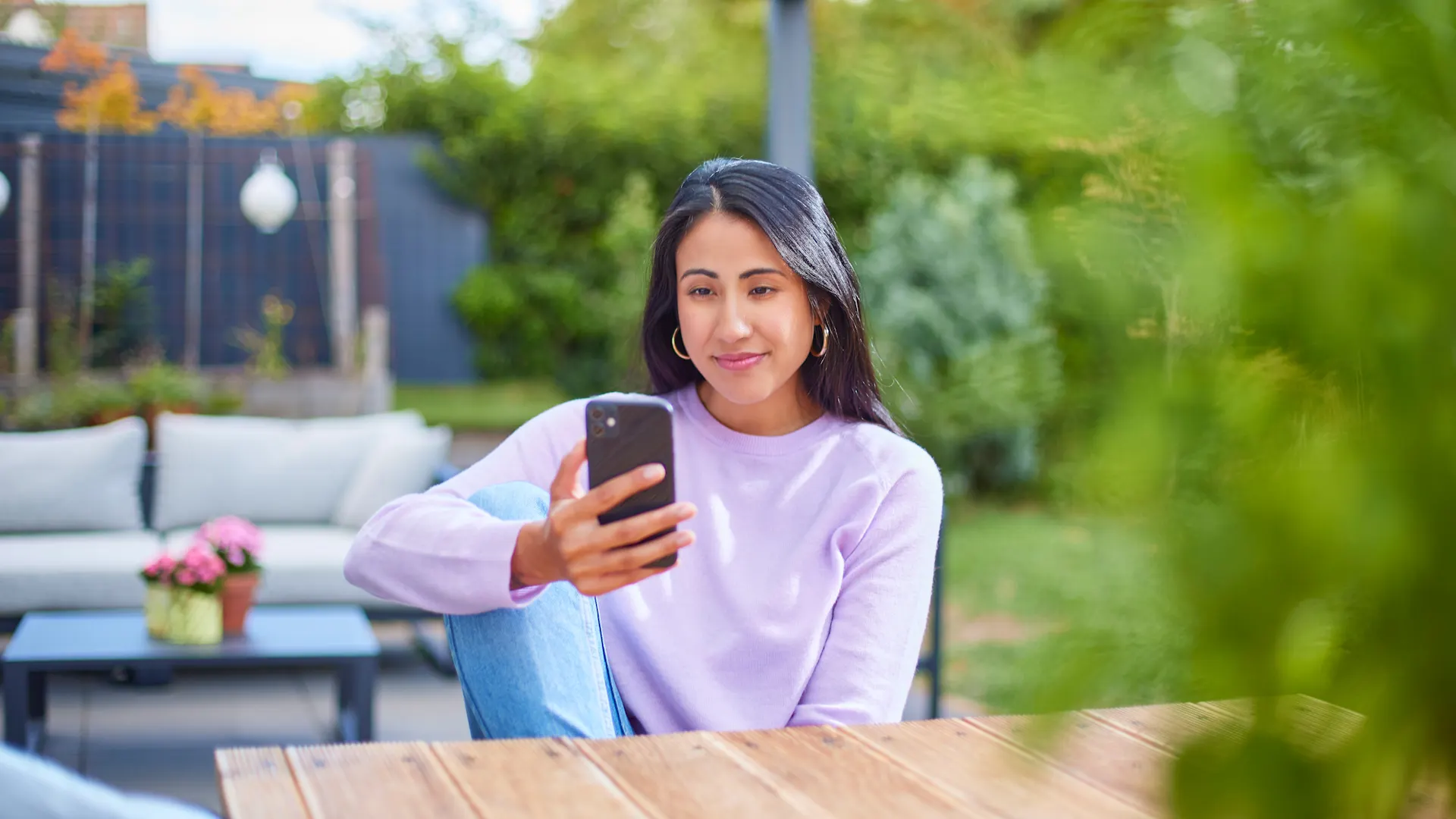 Frau mit Smartphone schaut nach günstigen Tarifen Eine Frau sitzt im Garten mit einem Smartphone und informiert sich über günstige Tarife und günstige Energie der NEW Energie.