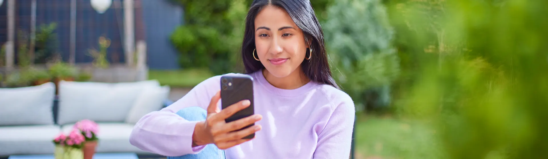 Frau mit Smartphone schaut nach günstigen Tarifen Eine Frau sitzt im Garten mit einem Smartphone und informiert sich über günstige Tarife und günstige Energie der NEW Energie.