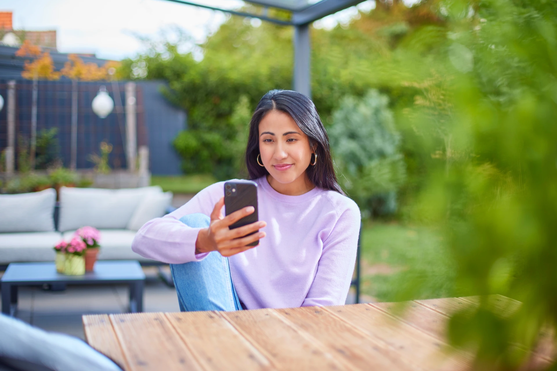 Eine Frau sitzt im Garten mit einem Smartphone und informiert sich über günstige Tarife und günstige Energie.