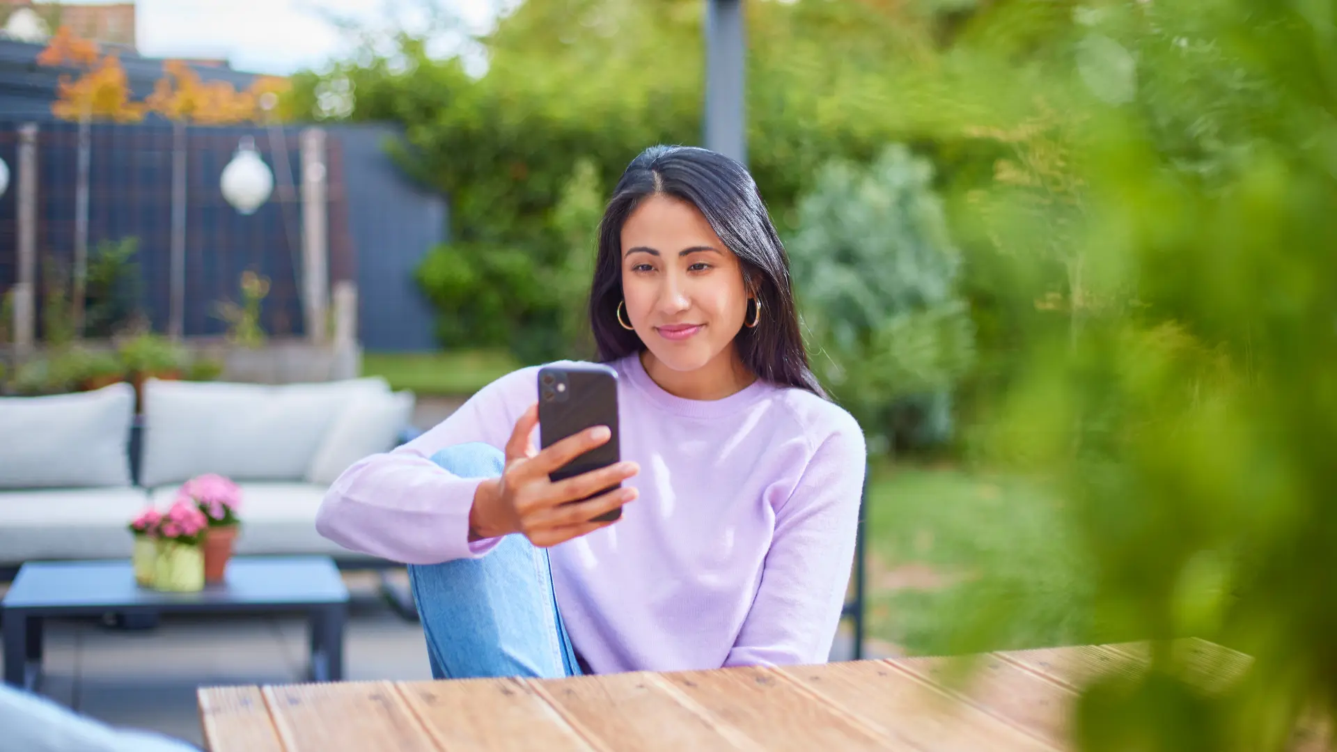 Eine Frau sitzt im Garten mit einem Smartphone und informiert sich über günstige Tarife und günstige Energie.