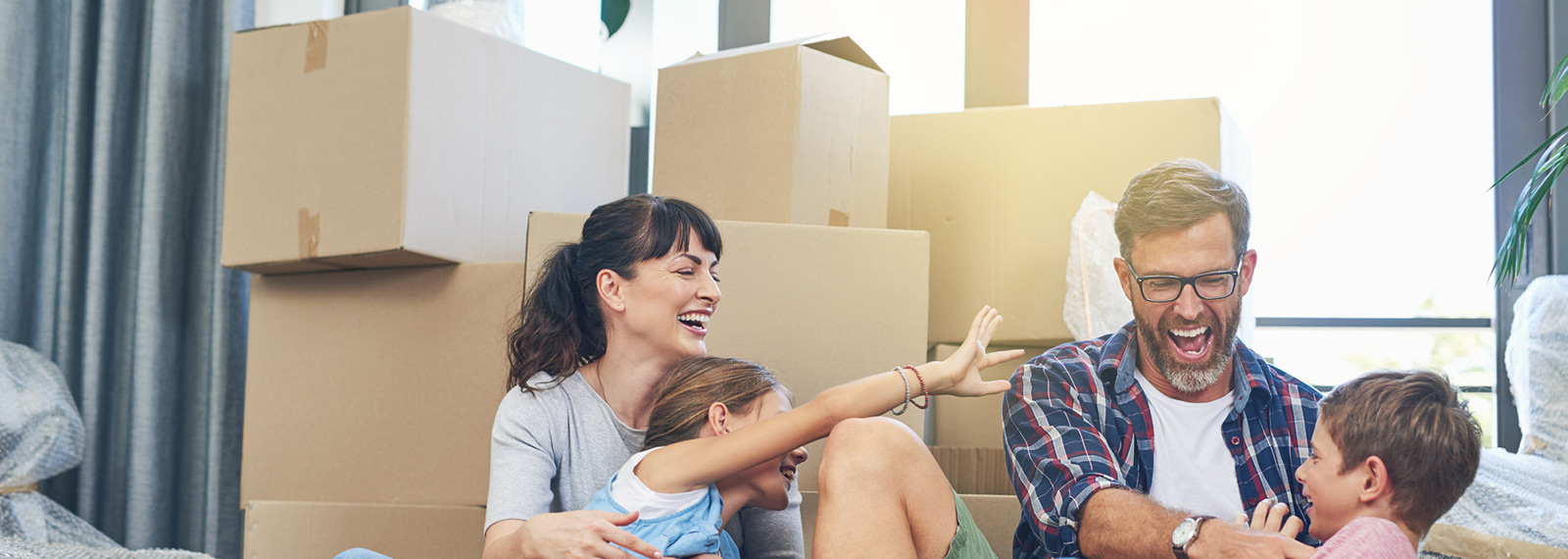 Eine Familie sitzt auf dem Boden vor Umzugskartons. Sie unterhalten sich darüber, auch am neuen Wohnort Energie durch die NEW Energie zu beziehen.