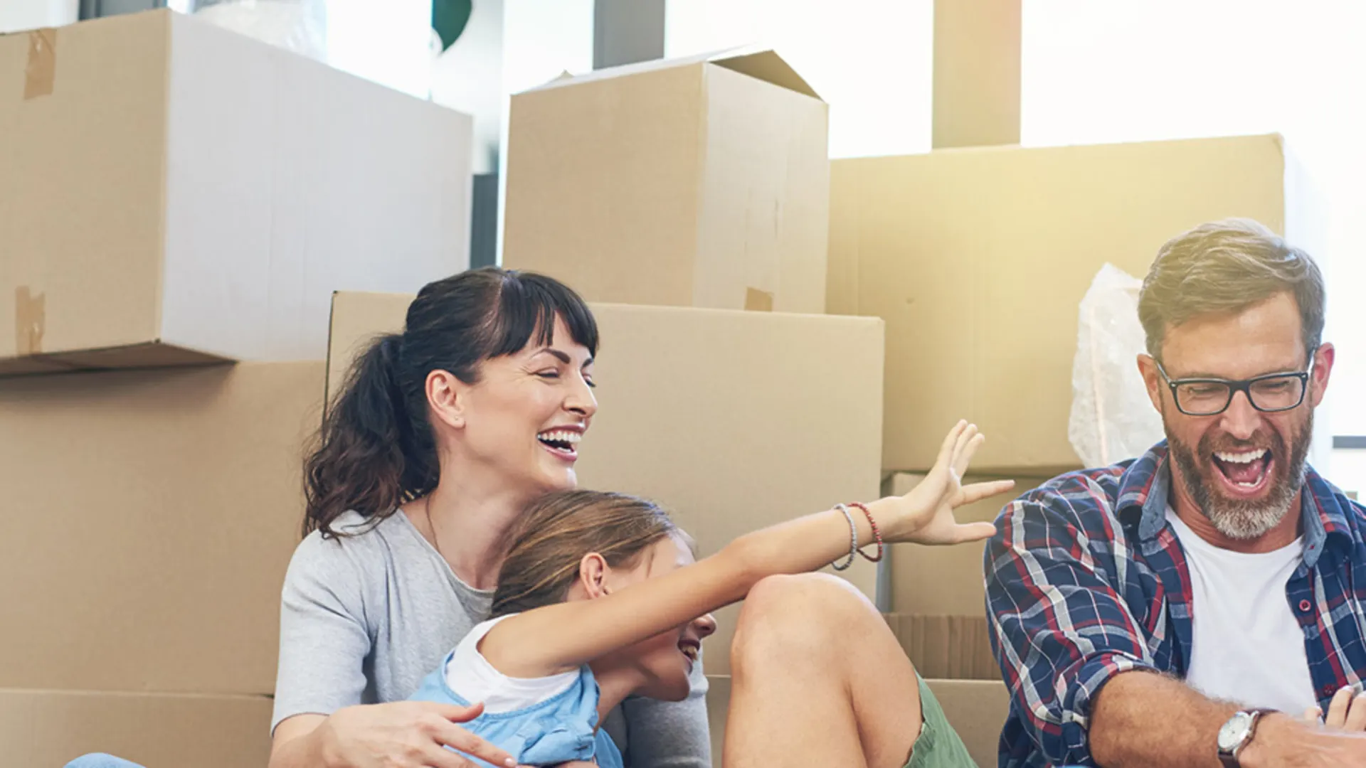Sie möchten umziehen? Wir ziehen mit. Eine Familie sitzt auf dem Boden vor Umzugskartons. Sie unterhalten sich darüber, auch am neuen Wohnort Energie durch die NEW Energie zu beziehen.