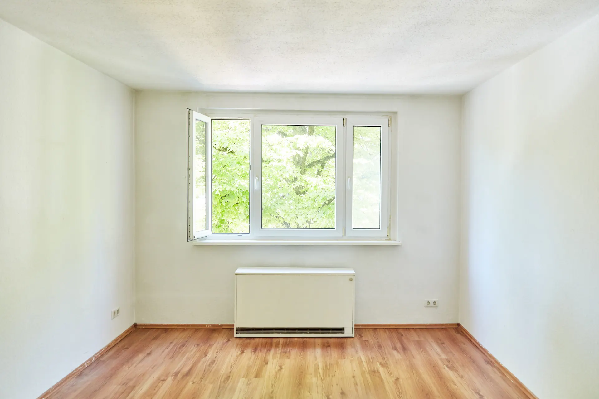 Eine Nachtspeicherheizung der NEW Energie steht in einem Zimmer unter einem Fenster.