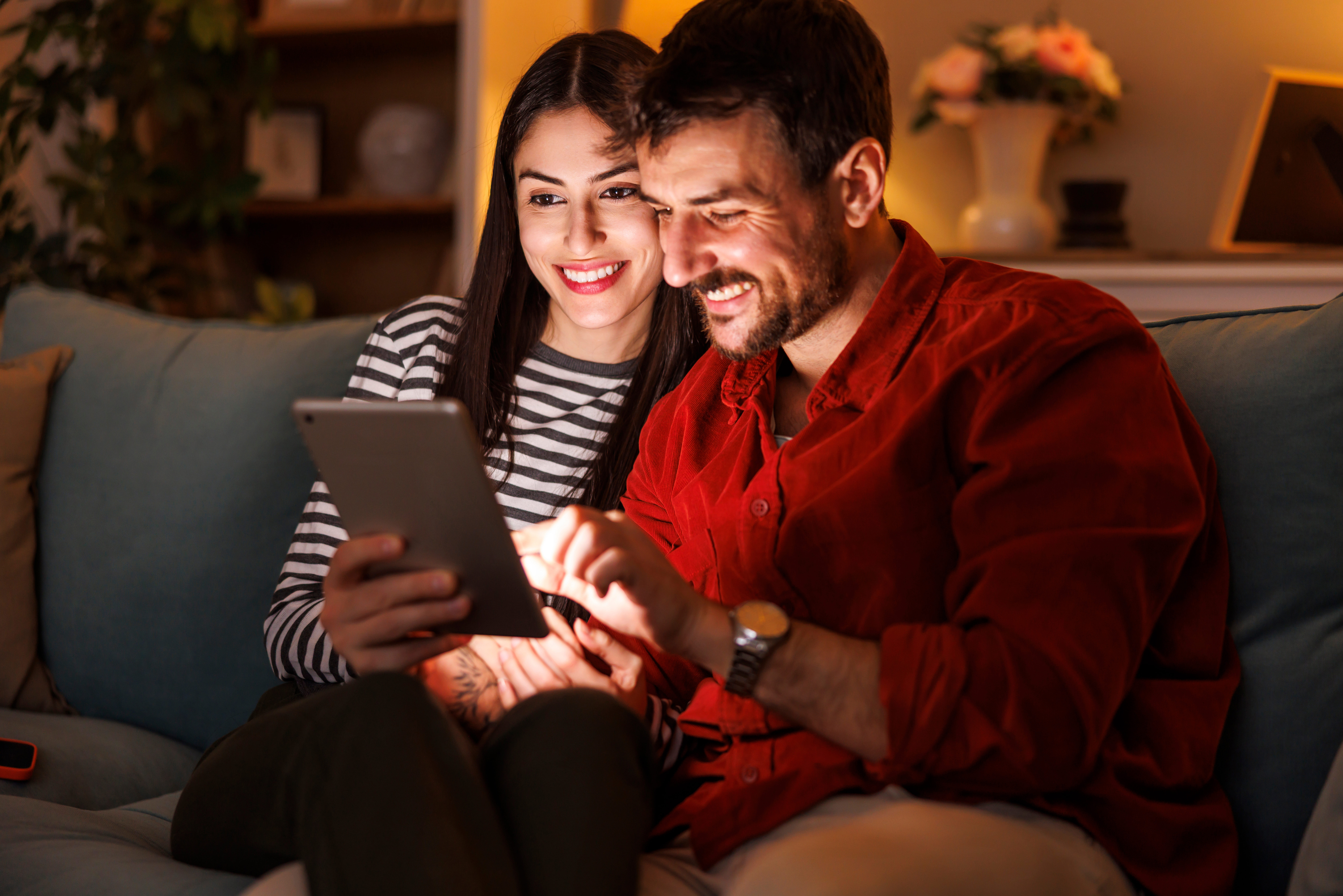 Ein Pärchen sitzt gemeinsam auf dem Sofa und schaut sich auf einem Tablet die attraktiven Angebote der NEW Energie an.