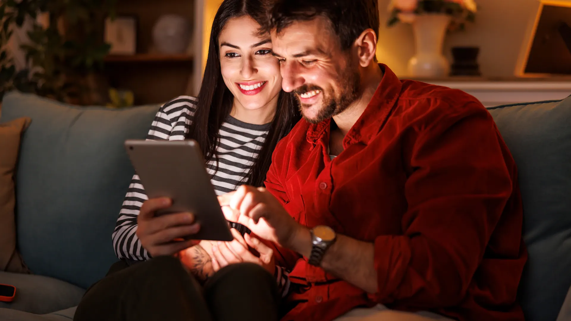 Jetzt zu der NEW Energie wechseln Ein Pärchen sitzt gemeinsam auf dem Sofa und schaut sich auf einem Tablet die attraktiven Angebote der NEW Energie an.