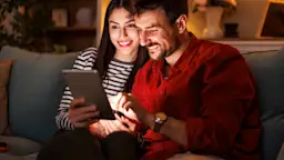Jetzt zu der NEW Energie wechseln Ein Pärchen sitzt gemeinsam auf dem Sofa und schaut sich auf einem Tablet die attraktiven Angebote der NEW Energie an.
