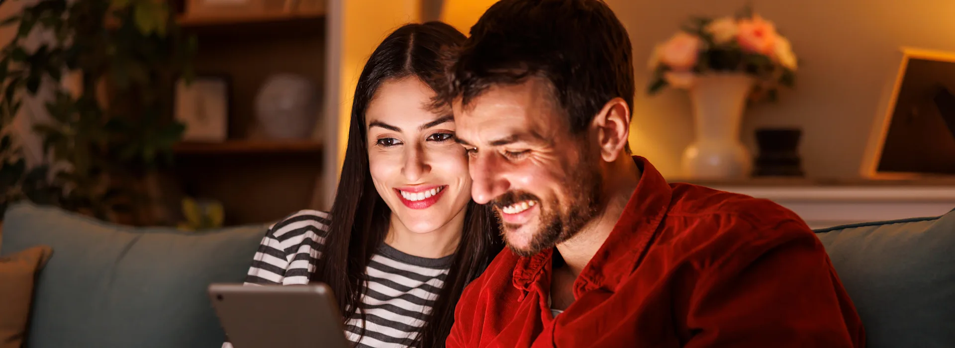 Jetzt zu der NEW Energie wechseln Ein Pärchen sitzt gemeinsam auf dem Sofa und schaut sich auf einem Tablet die attraktiven Angebote der NEW Energie an.
