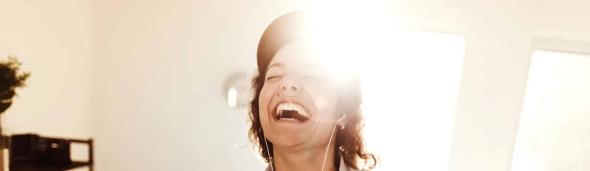 Frühjahrsdeal der NEW Energie für Strom und Gas Frau steht lachend im Wohnzimmer und hört Musik über Kopfhörer. Sie freut sich über die Angebote der NEW Energie.