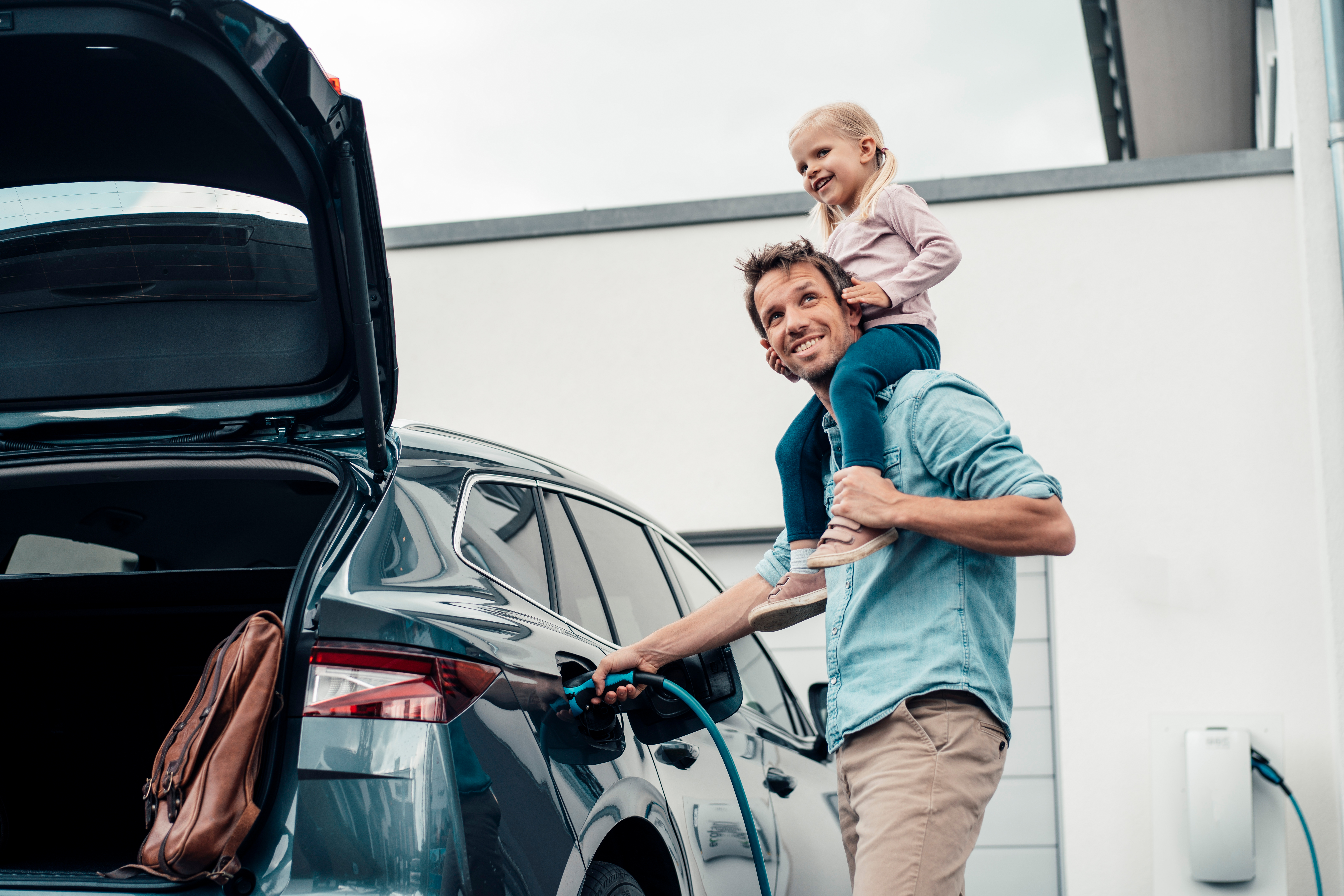Ein Kind sitzt beim Vater auf den Schultern während der Vater das E-Auto mit Ökostrom der NEW Energie lädt.
