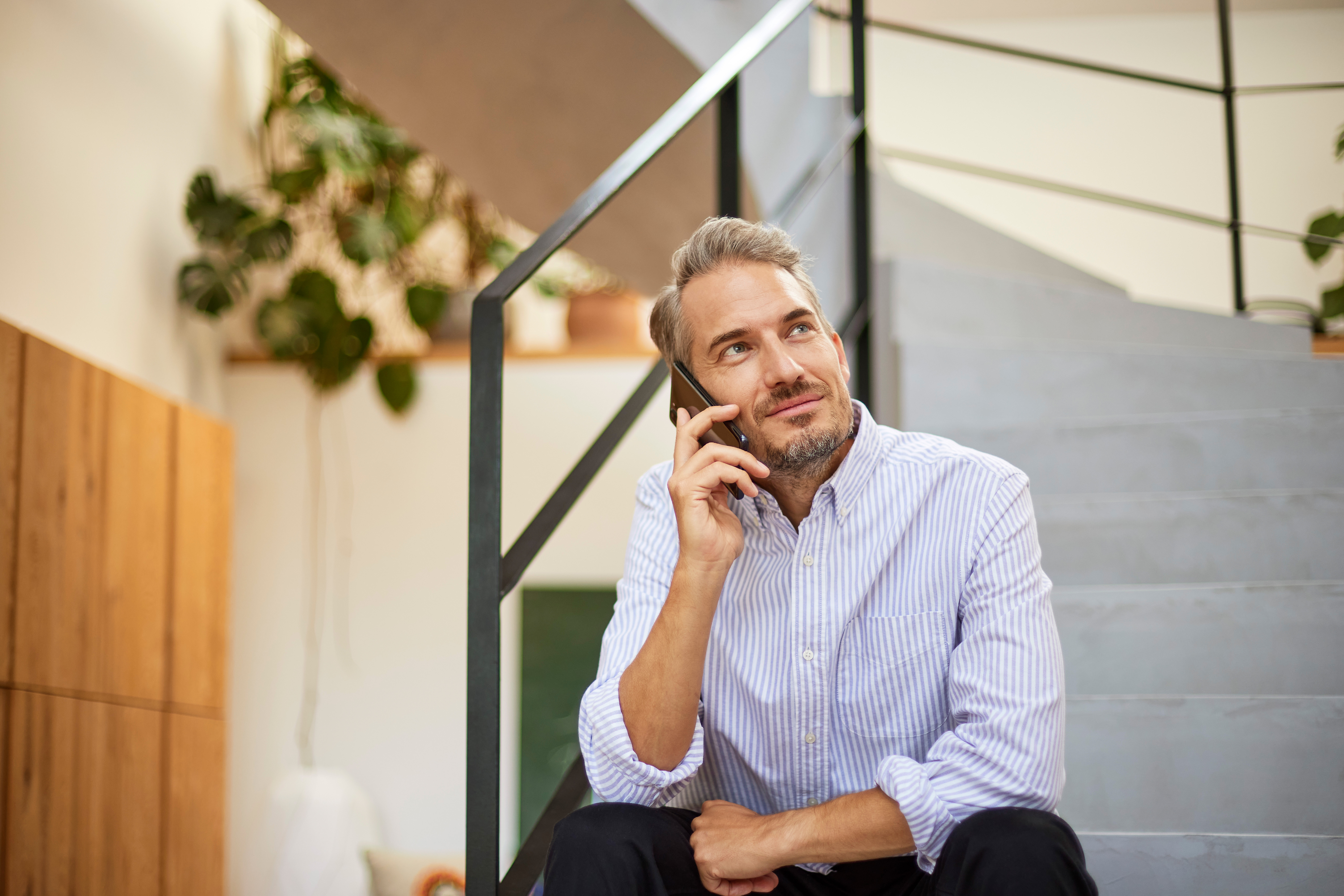 Ein Mann sitzt auf einer Treppe mit seinem Smartphone und kontaktiert den Kundenservice von dem Stromanbieter NEW Energie.