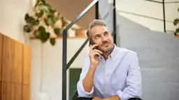 Mann mit Smartphone kontaktiert den Kundenservice der NEW Ein Mann sitzt auf einer Treppe mit seinem Smartphone und kontaktiert den Kundenservice von dem Stromanbieter NEW Energie.