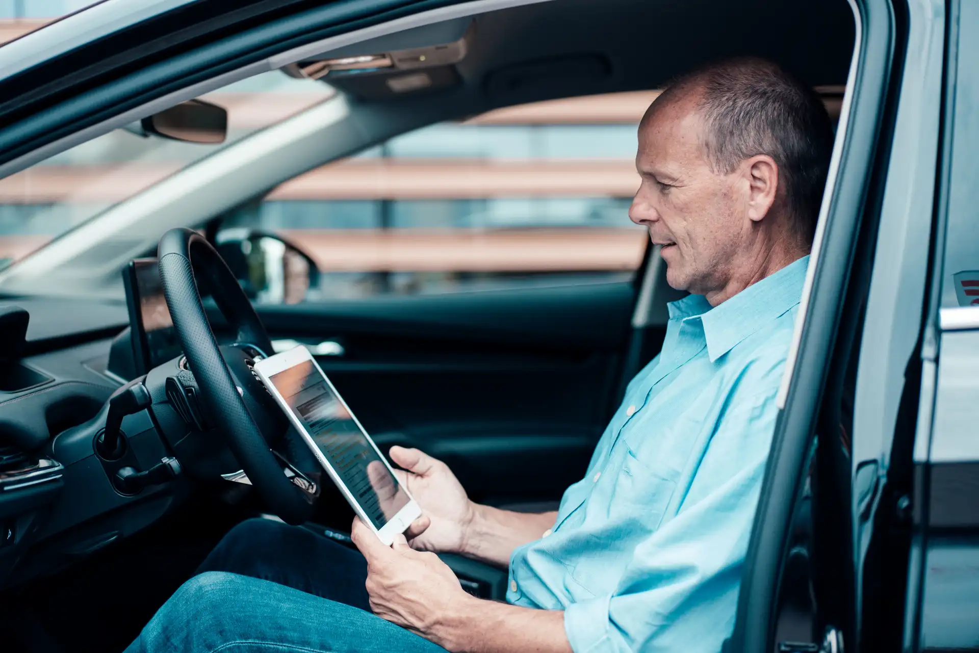 Mann schaut im Auto auf sein Tablet und informiert sich über das Lademanagement der NEW Energie.