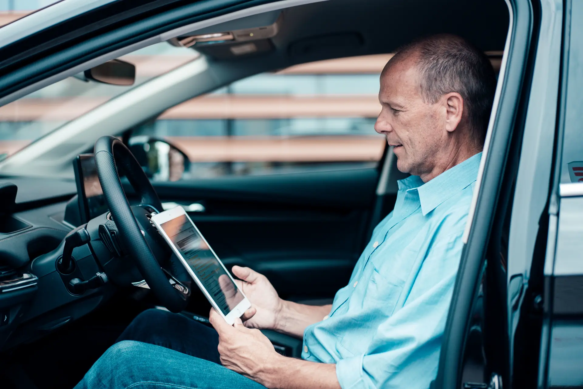 Mann schaut im Auto auf sein Tablet und informiert sich über das Lademanagement der NEW Energie.