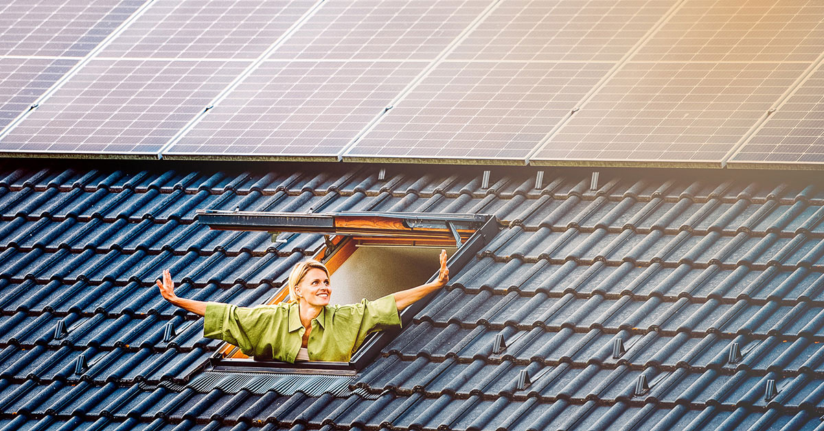 Eine Frau schaut strahlend aus dem Fenster. Über dem Fenster sind PV-Anlagen der NEW Energie montiert.