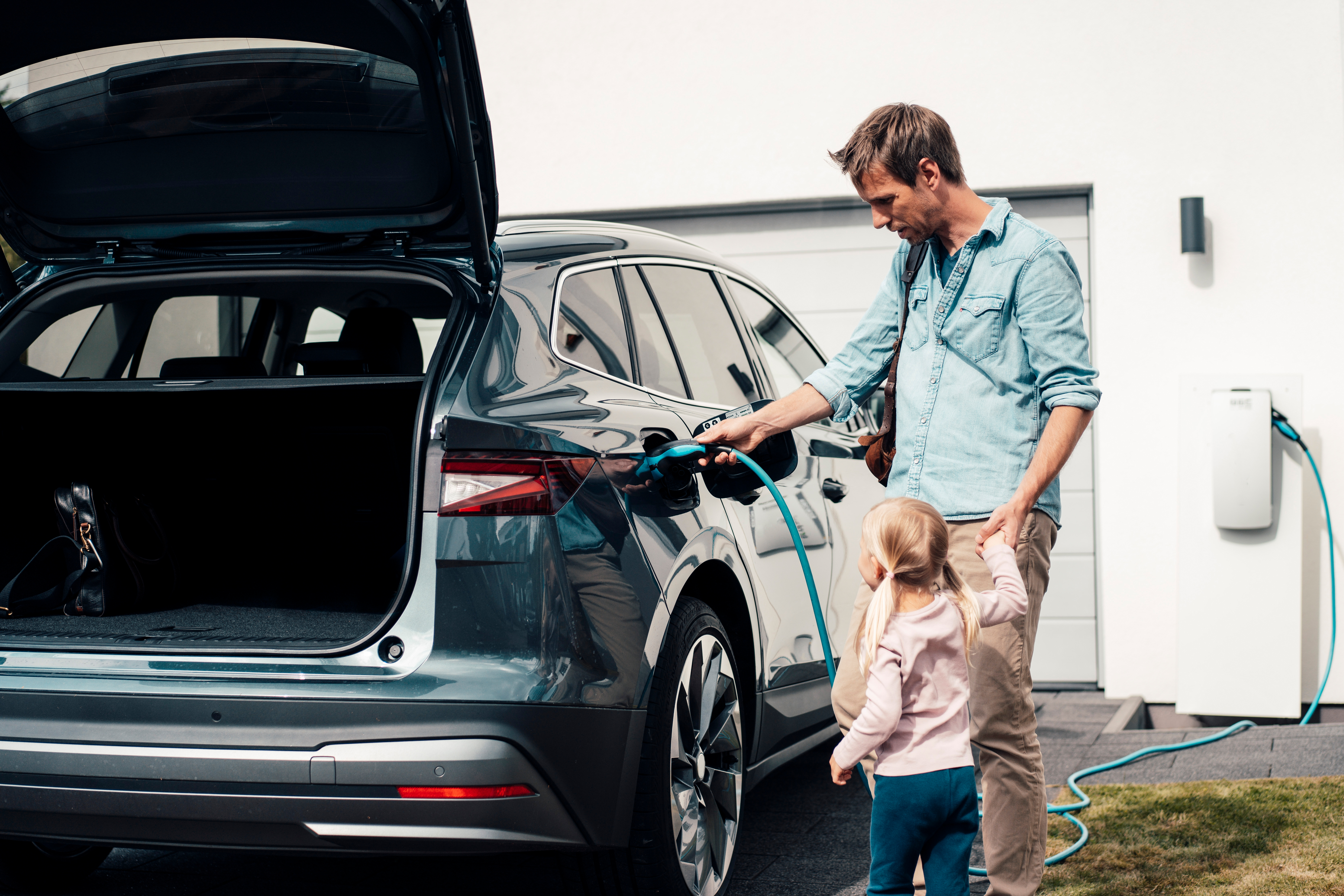 Ein Mann steckt ein Ladekabel in sein E-Auto. Sein Auto wird Strom von der NEW Energie geladen.