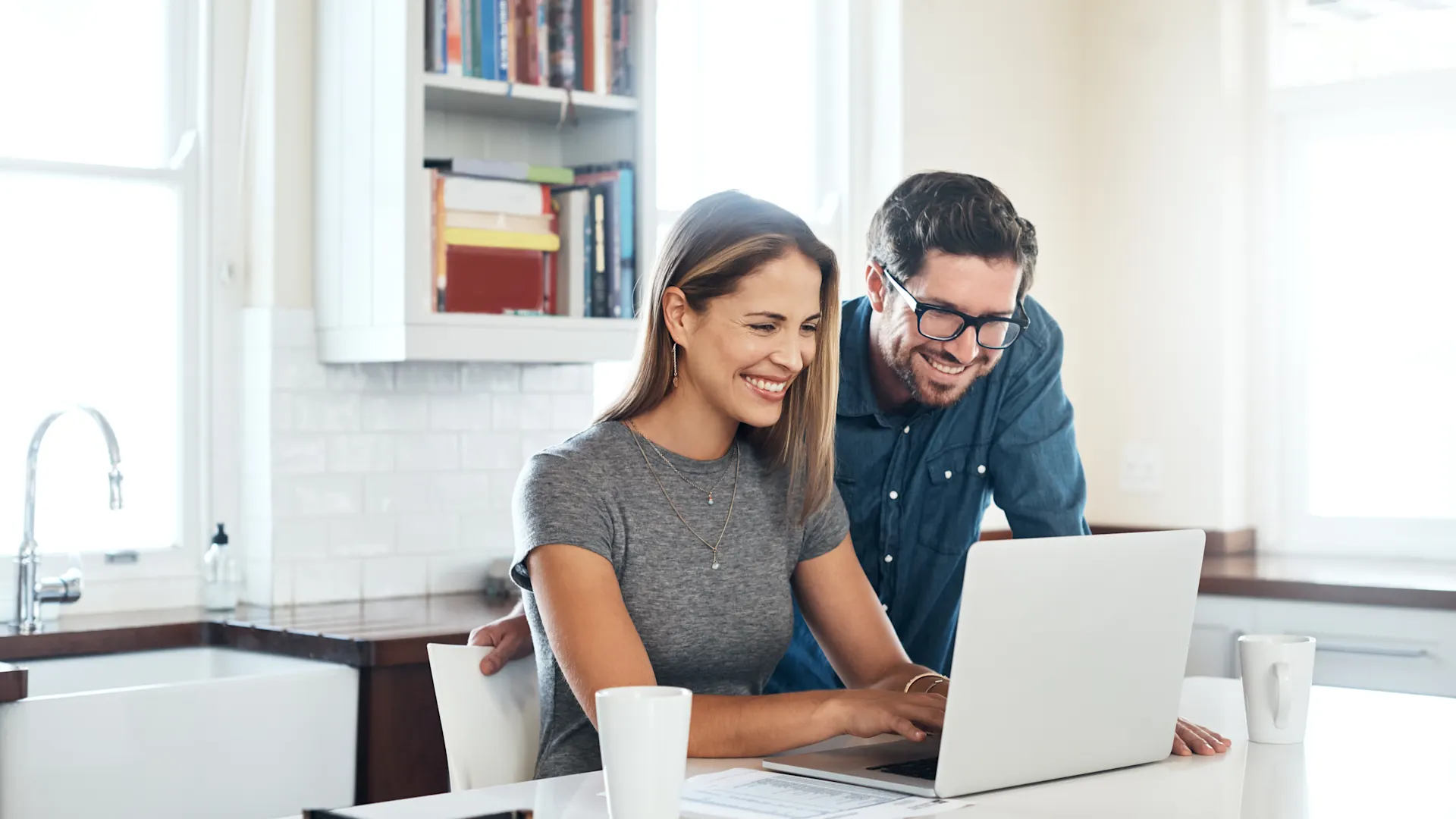 Strompreise vergleichen Ein Mann und eine Frau sitzen an einem Laptop in einer Küche und vergleichen die Strompreise der NEW Energie.