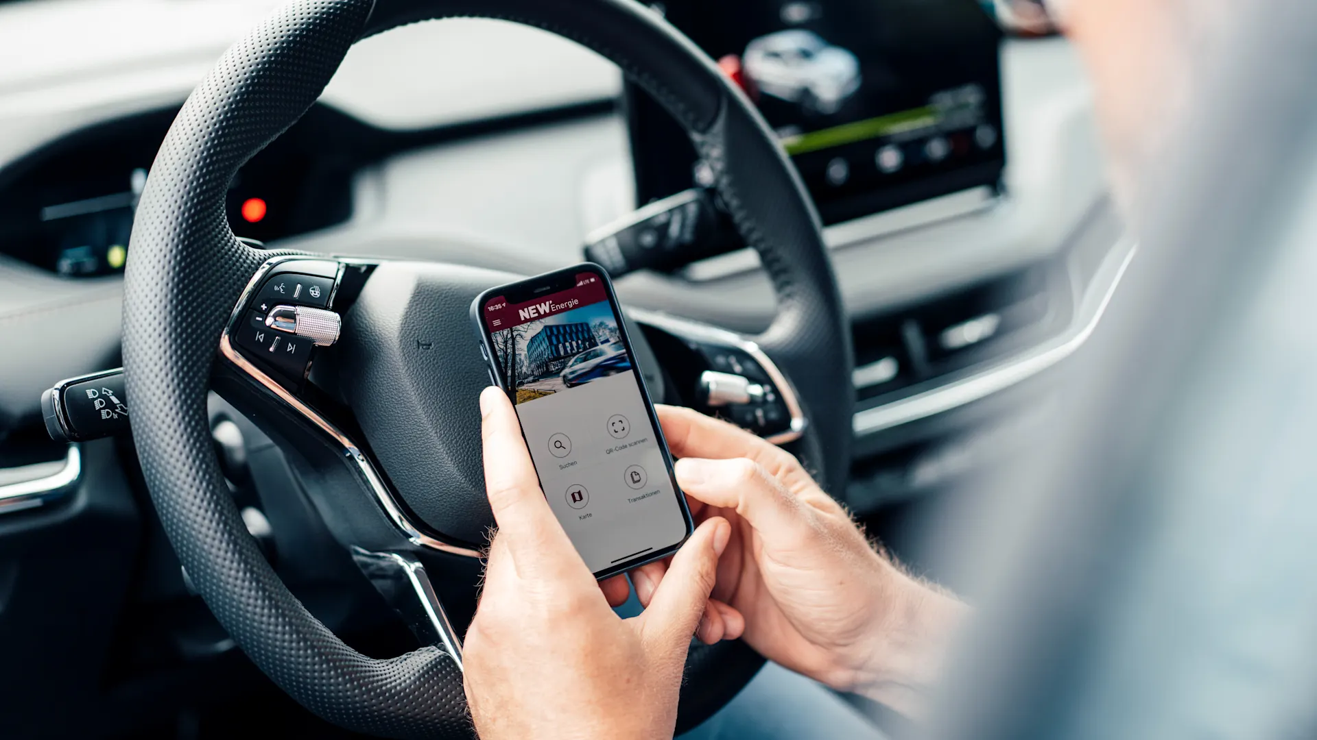 App fürs E-Auto Ein Mann sitzt in seinem Auto und hält ein Smartphone in der Hand und schaut sich eine App der NEW Energie an.