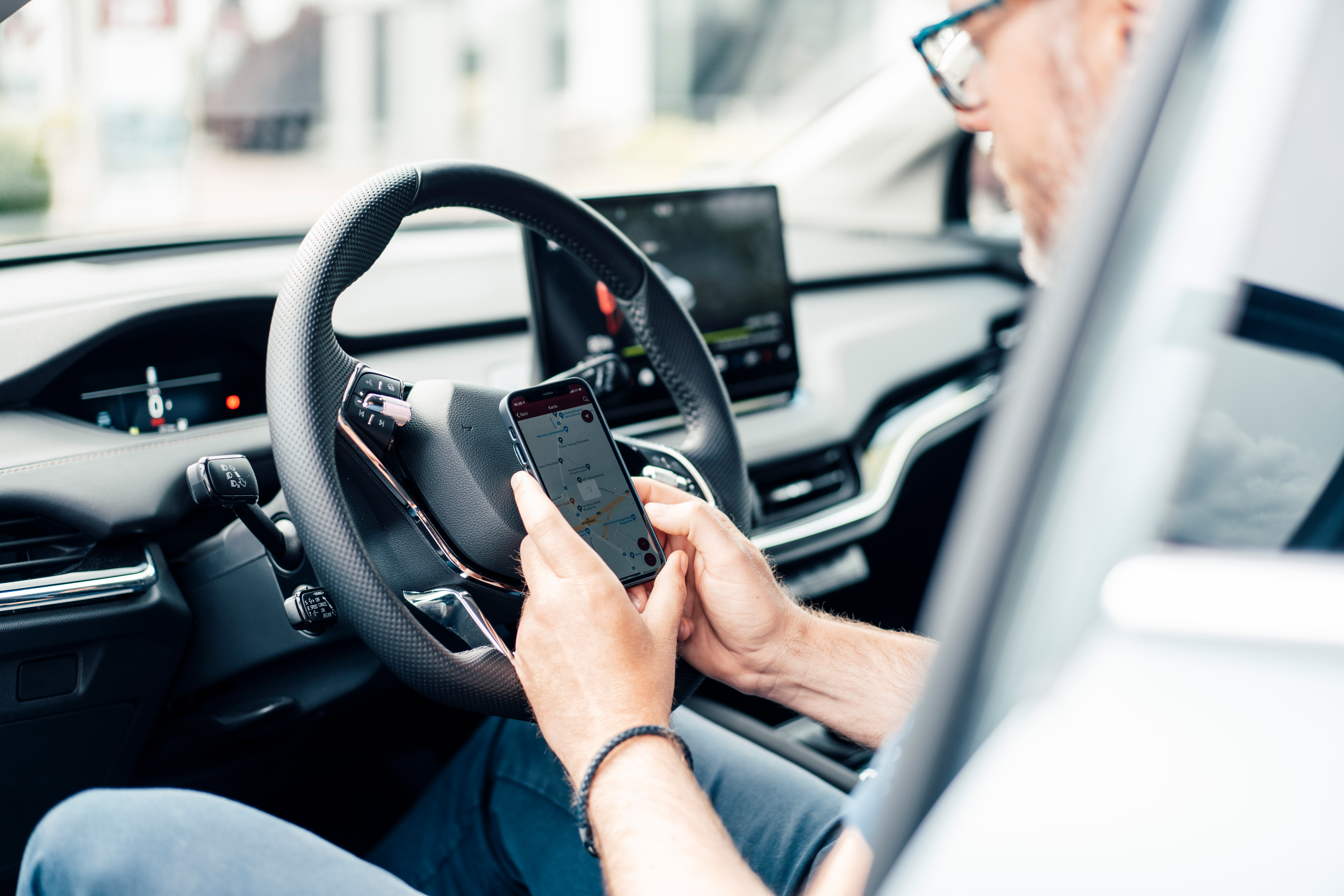 Mann sitzt in einem Auto bei geöffneter Autotür und prüft Ladevorgang seines Autos in der NEW-App.