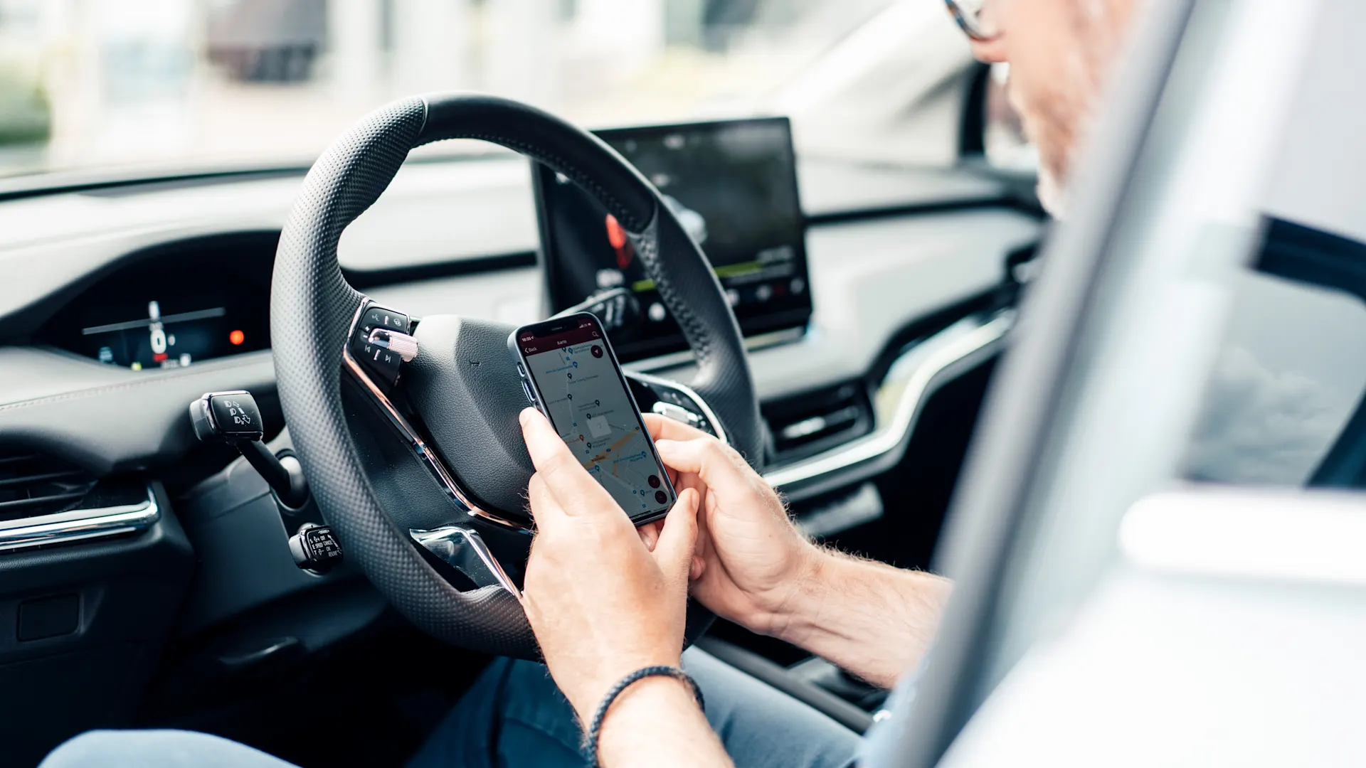 App für E-Autos Mann sitzt in einem Auto bei geöffneter Autotür und prüft Ladevorgang seines Autos in der NEW-App.