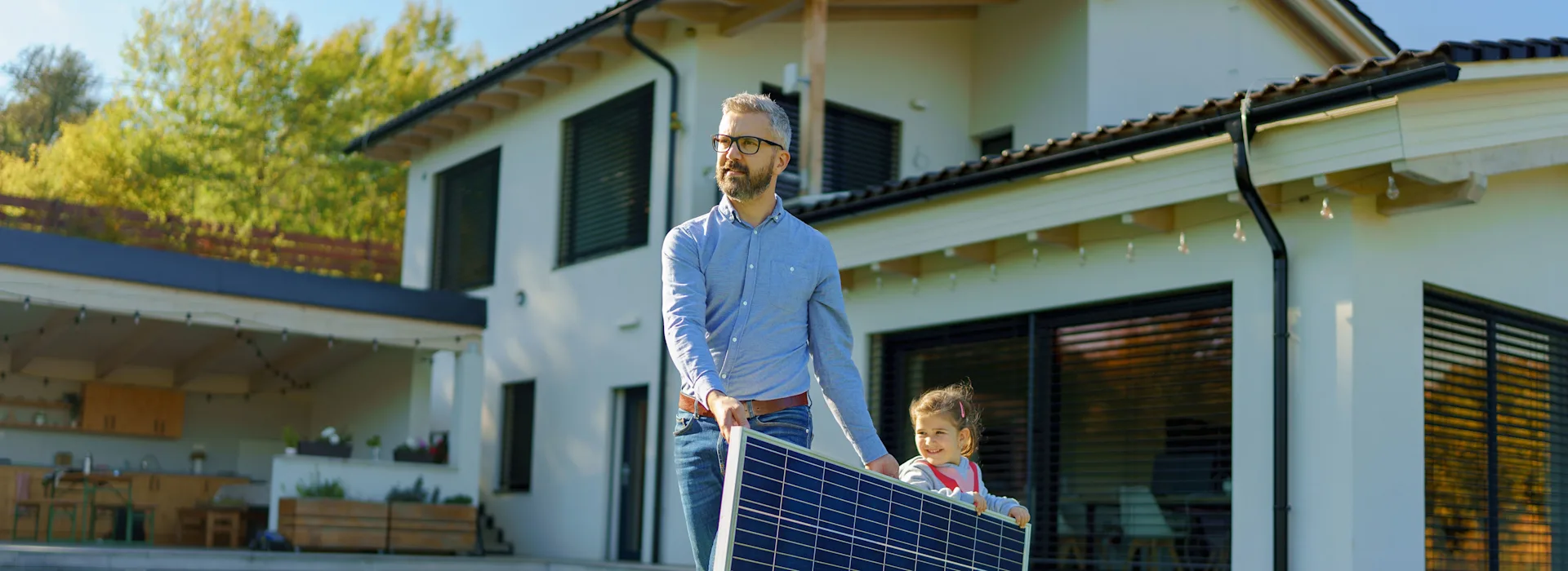 Vater und Tochter tragen PV Modul der NEW Energie Vater und Tochter tragen ein PV Modul der NEW Energie durch den Garten ihres Einfamilienhauses.