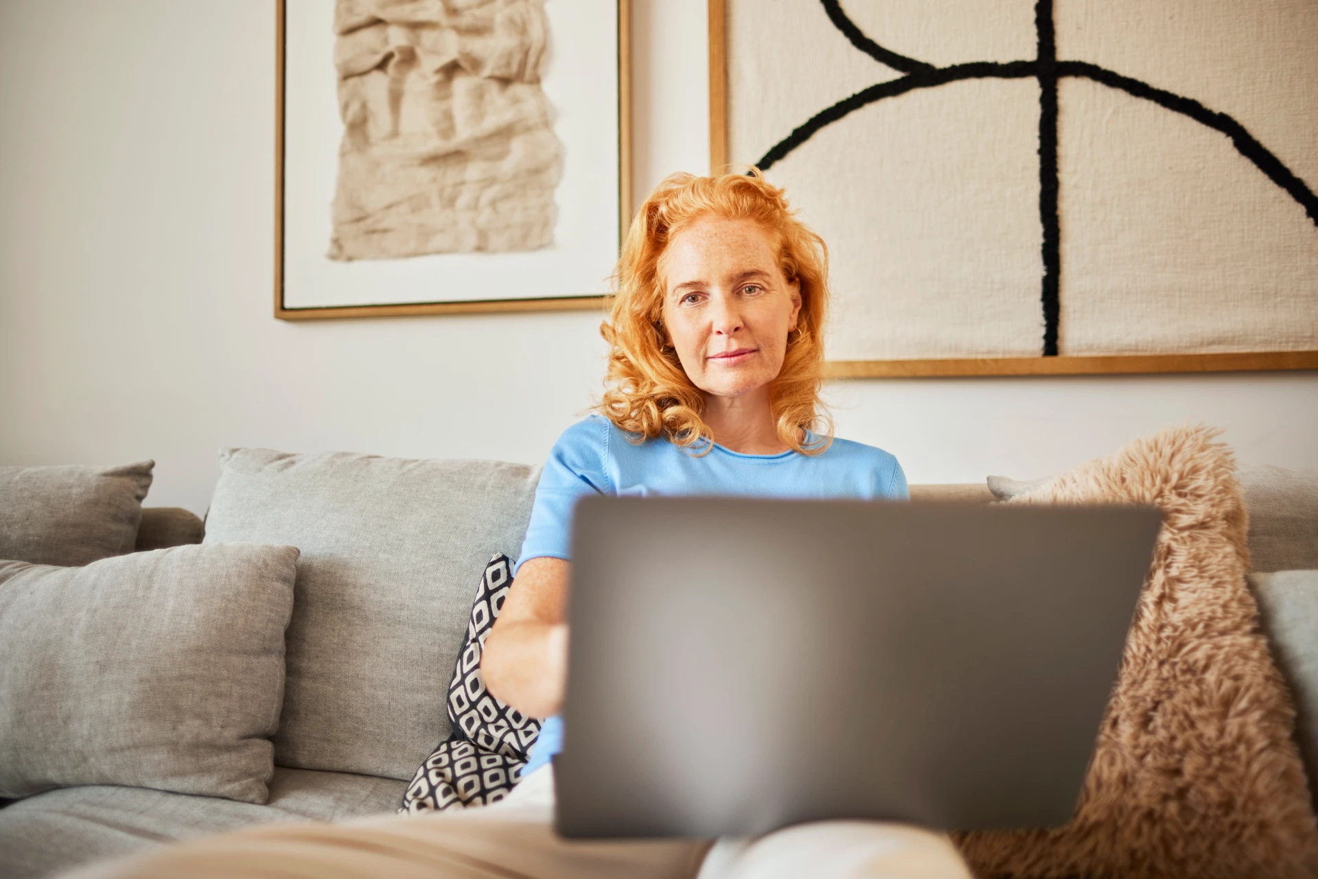 Eine Frau sitzt mit ihrem Laptop auf dem Sofa und informiert sich über die Auswahl an günstiger Energie der NEW Energie.