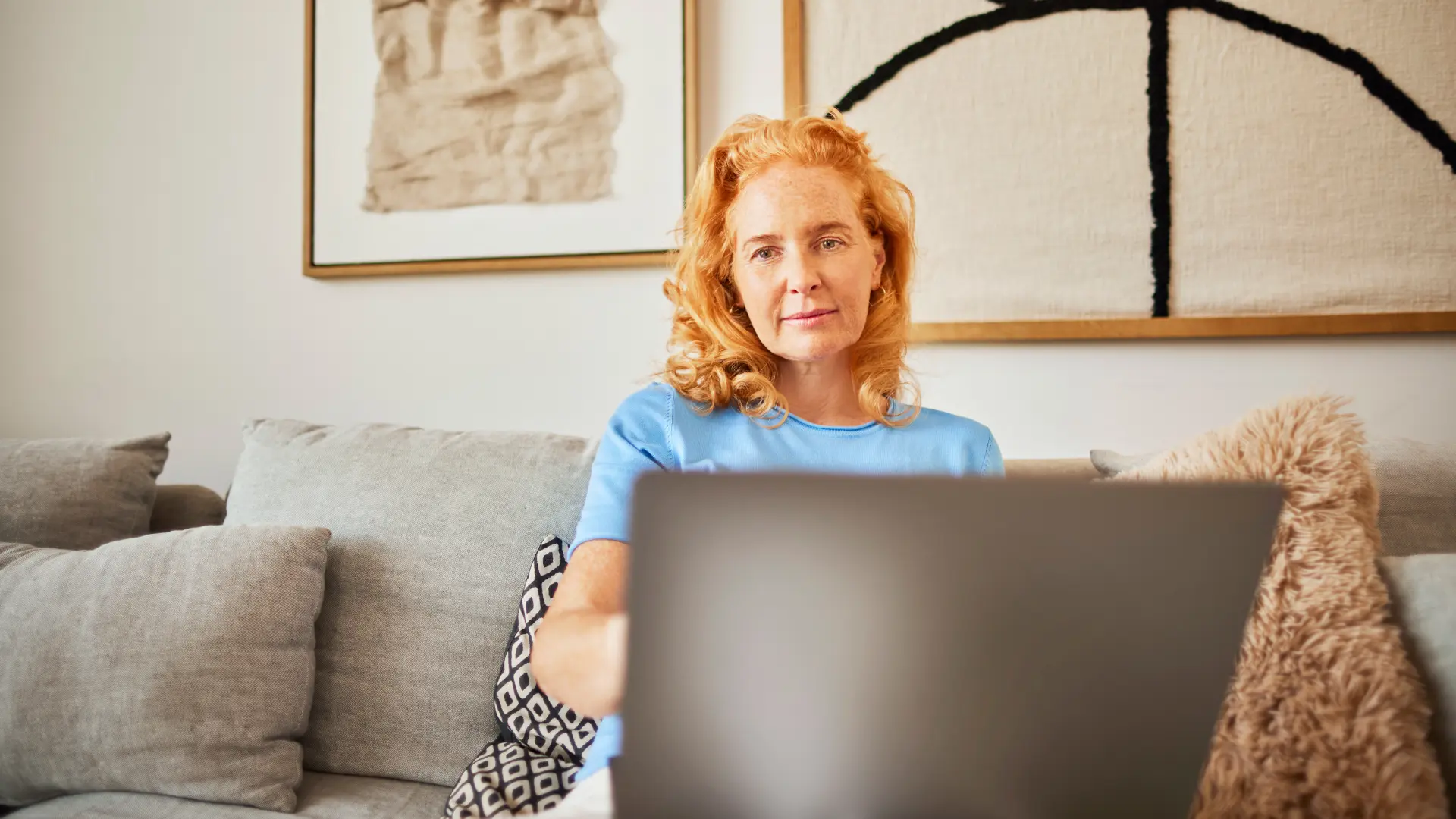 Eine Frau sitzt mit ihrem Laptop auf dem Sofa und informiert sich über die Auswahl an günstiger Energie der NEW Energie.