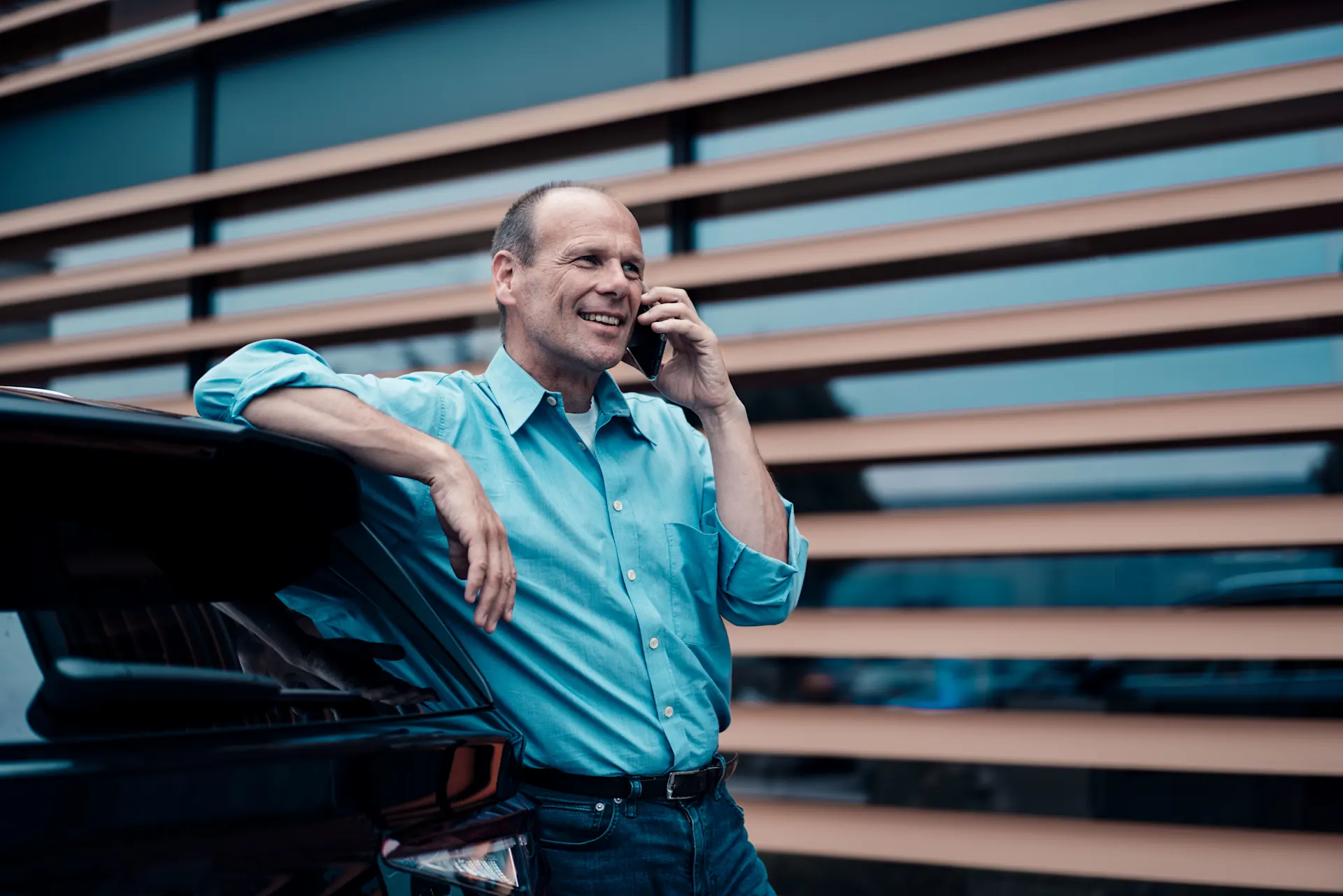 Unternehmer steht am E-Auto und telefoniert.
