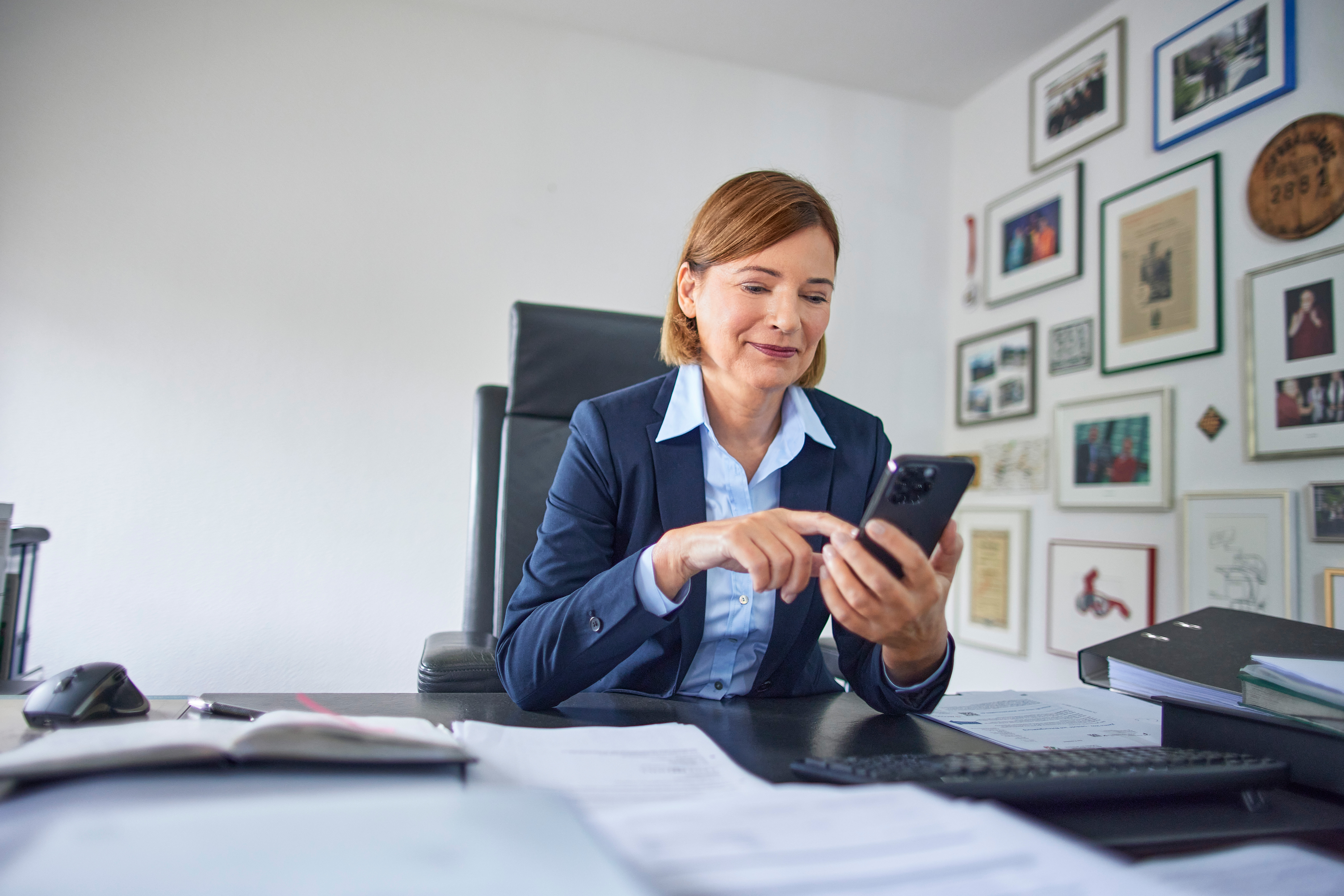 Eine Geschäftsführerin sitzt im Büro und schaut nach dem Service der NEW Energie auf ihrem Handy.