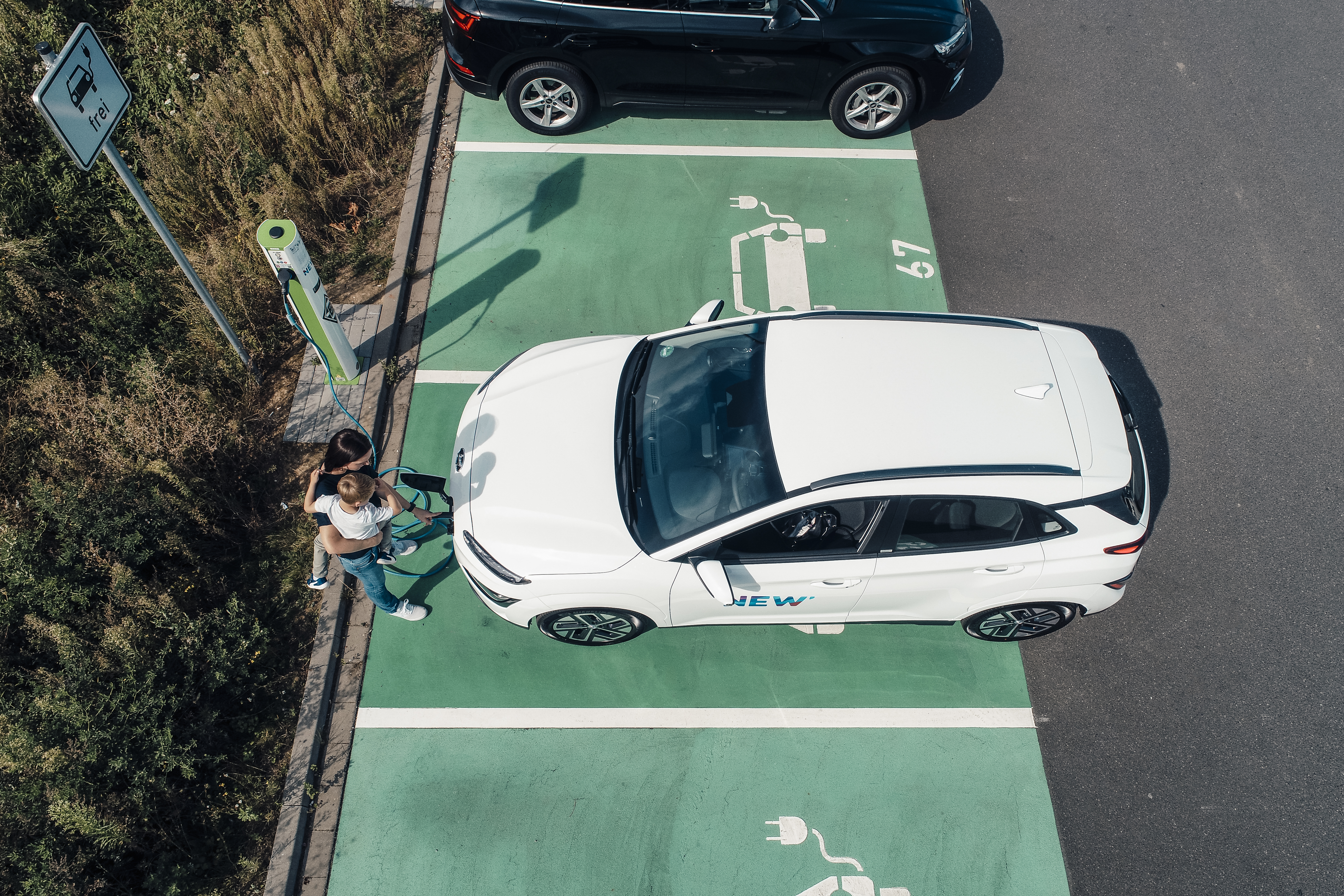 Kind sitzt während das Auto an einer Ladestation der NEW Energie lädt bei der Mutter auf dem Arm.